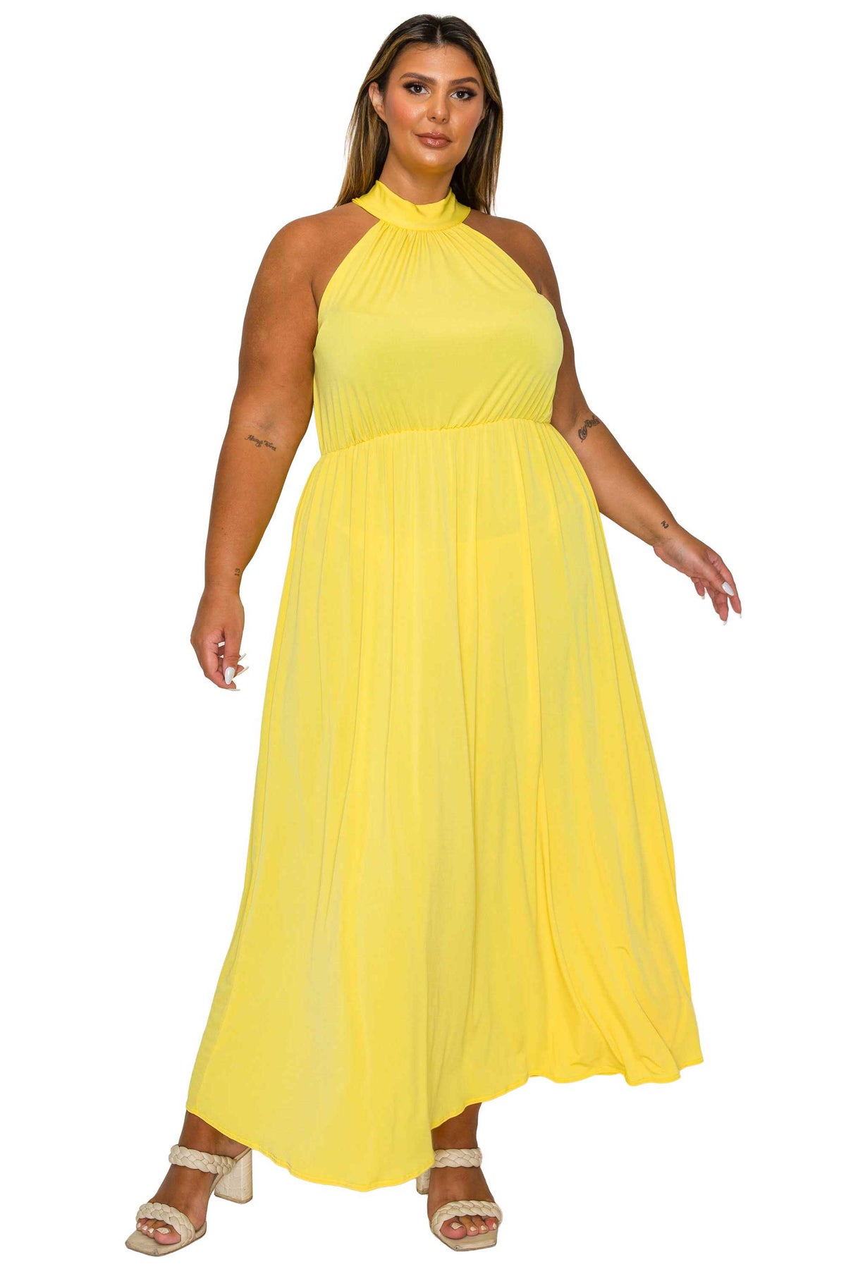 A woman modeling a bright yellow halter-neck maxi dress with a pleated skirt, paired with beige heeled sandals, against a plain white background.