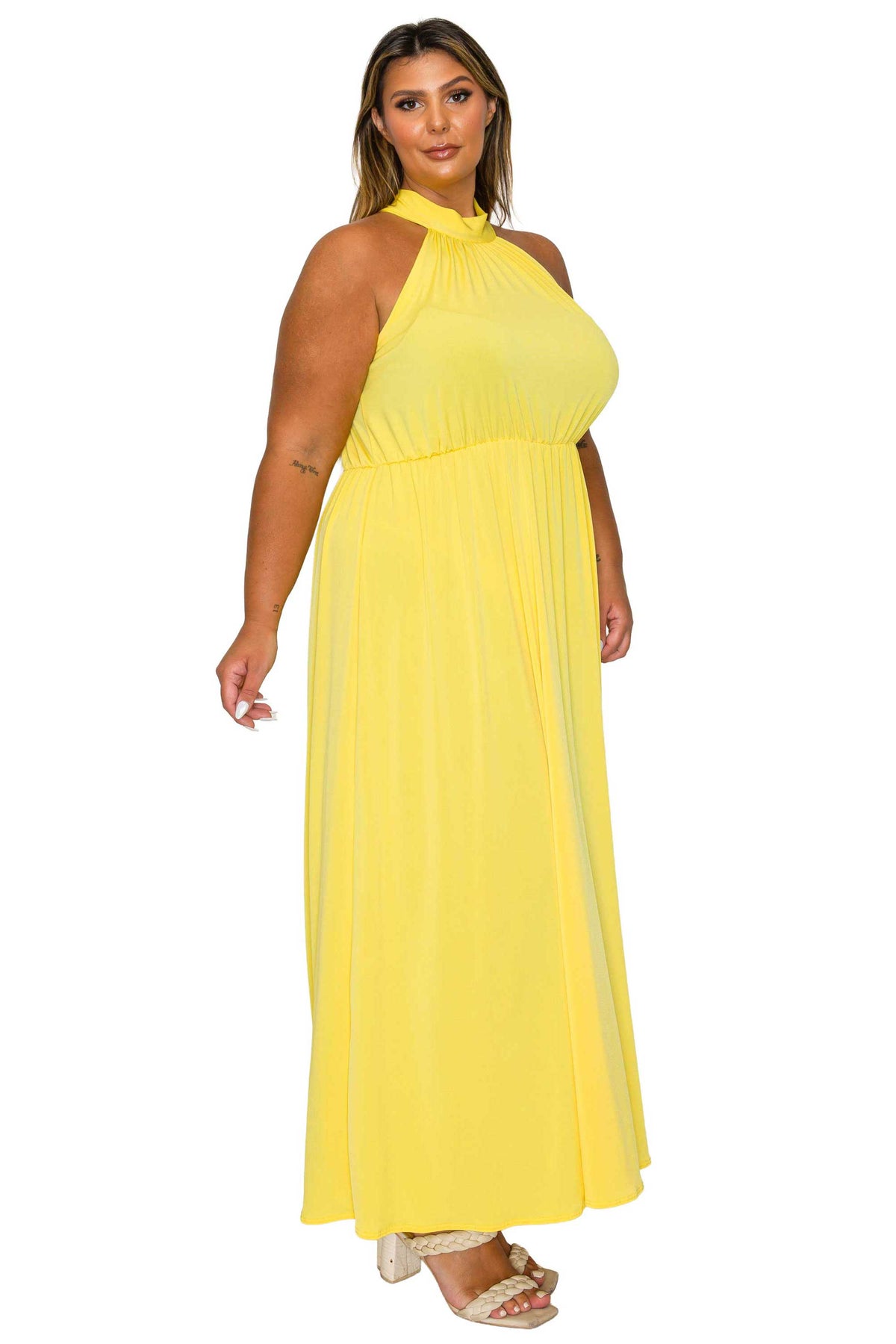 A woman modeling a bright yellow halter-neck maxi dress with a gathered waist and flowing skirt, paired with beige heeled sandals, against a plain white background.