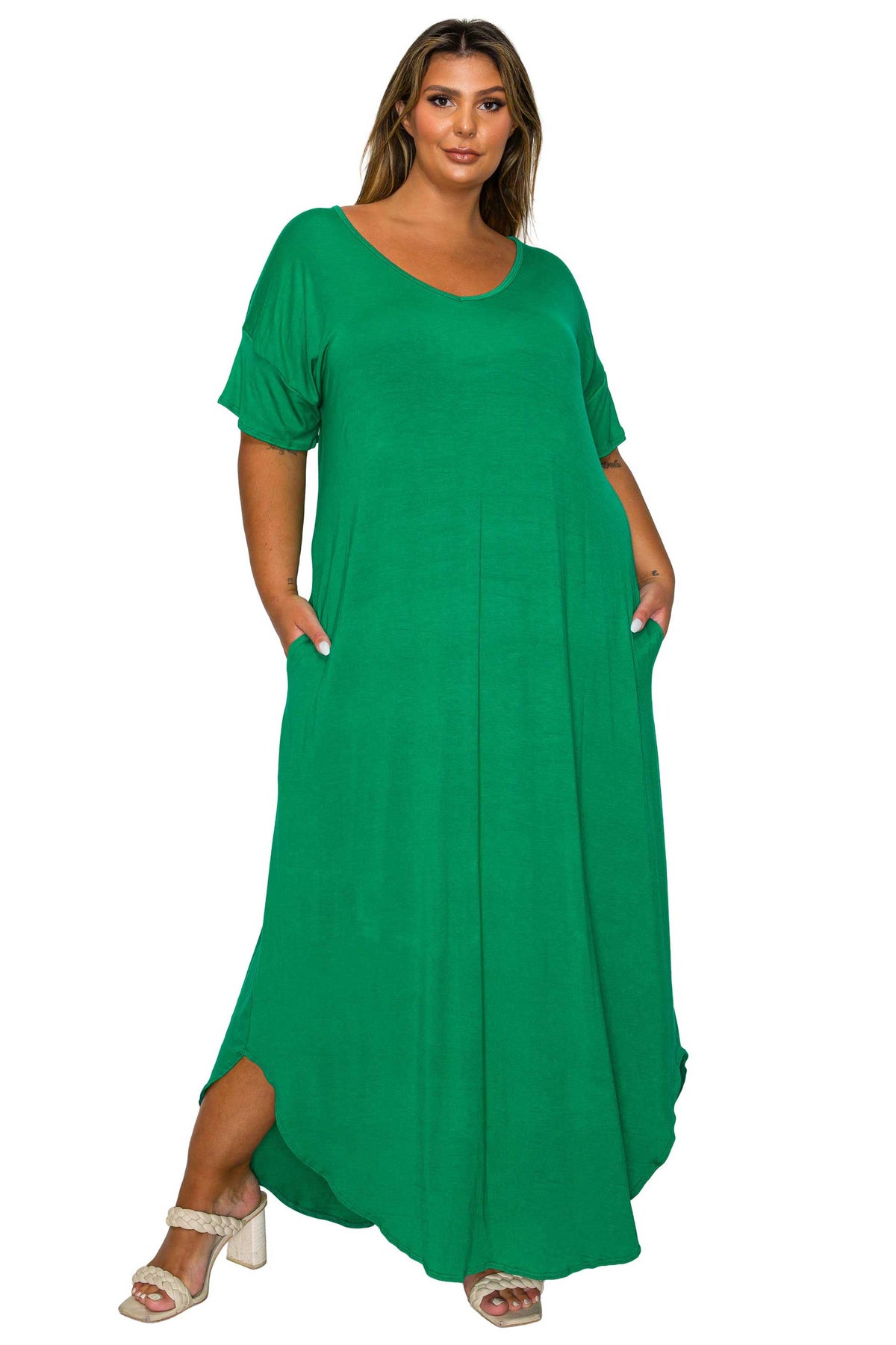 A woman modeling a bright green, short-sleeved maxi dress with side pockets, paired with white heeled sandals, against a plain white background.
