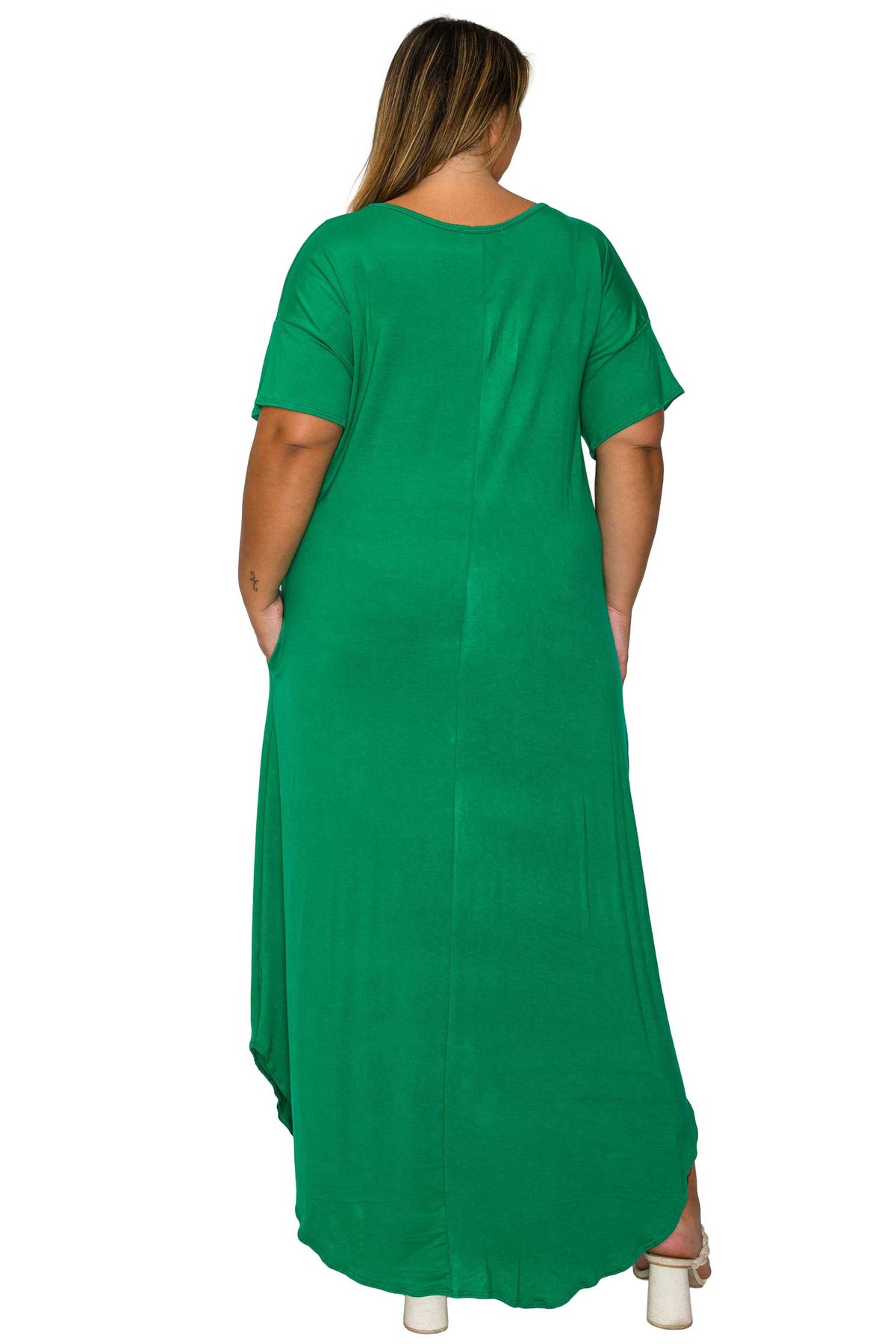 A woman viewed from the back wearing a bright green short-sleeve maxi dress with side pockets, paired with white high-heeled sandals, against a plain white background.