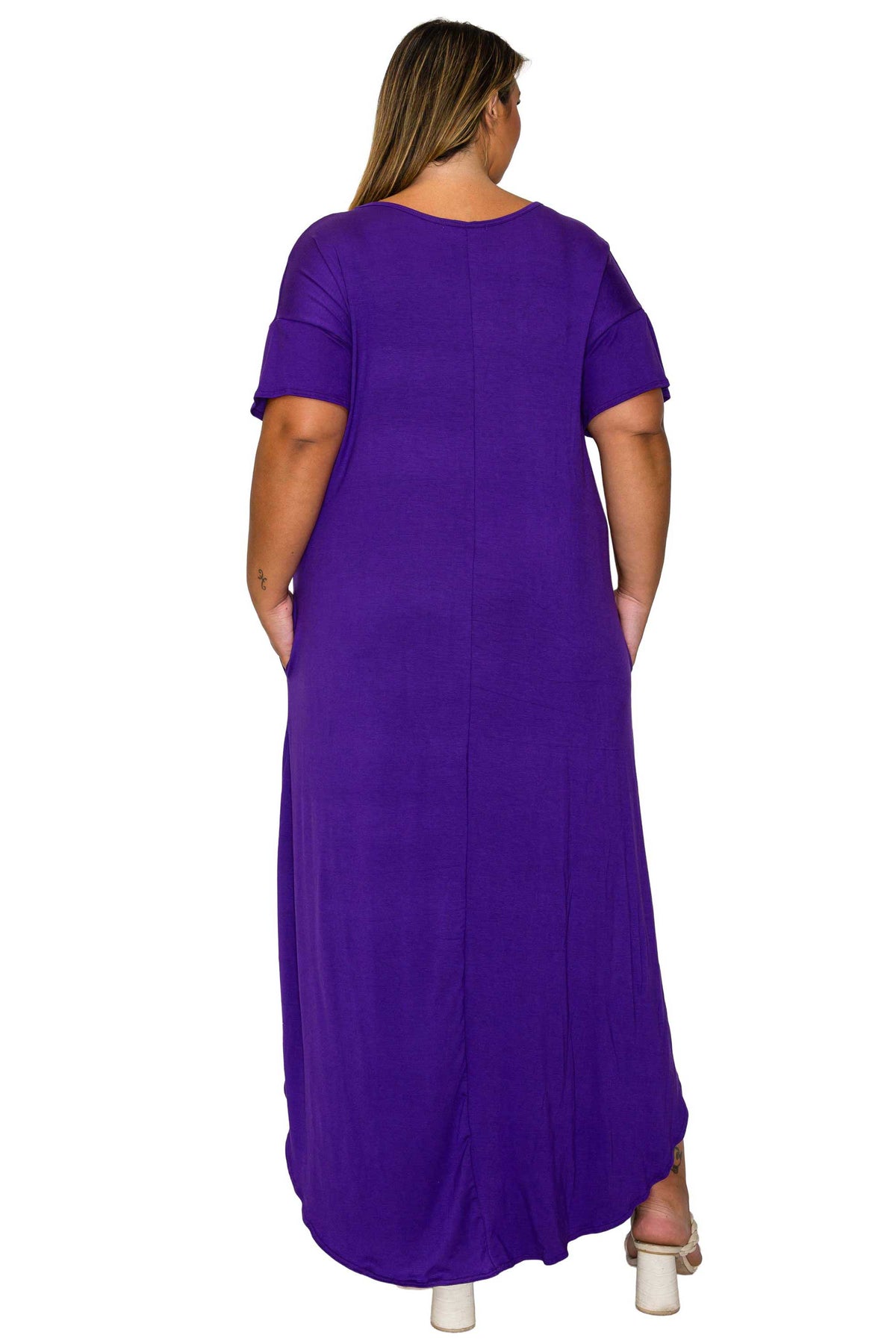 A woman viewed from the back wearing a loose, short-sleeve maxi dress in solid purple, paired with white high heels, against a plain white background.