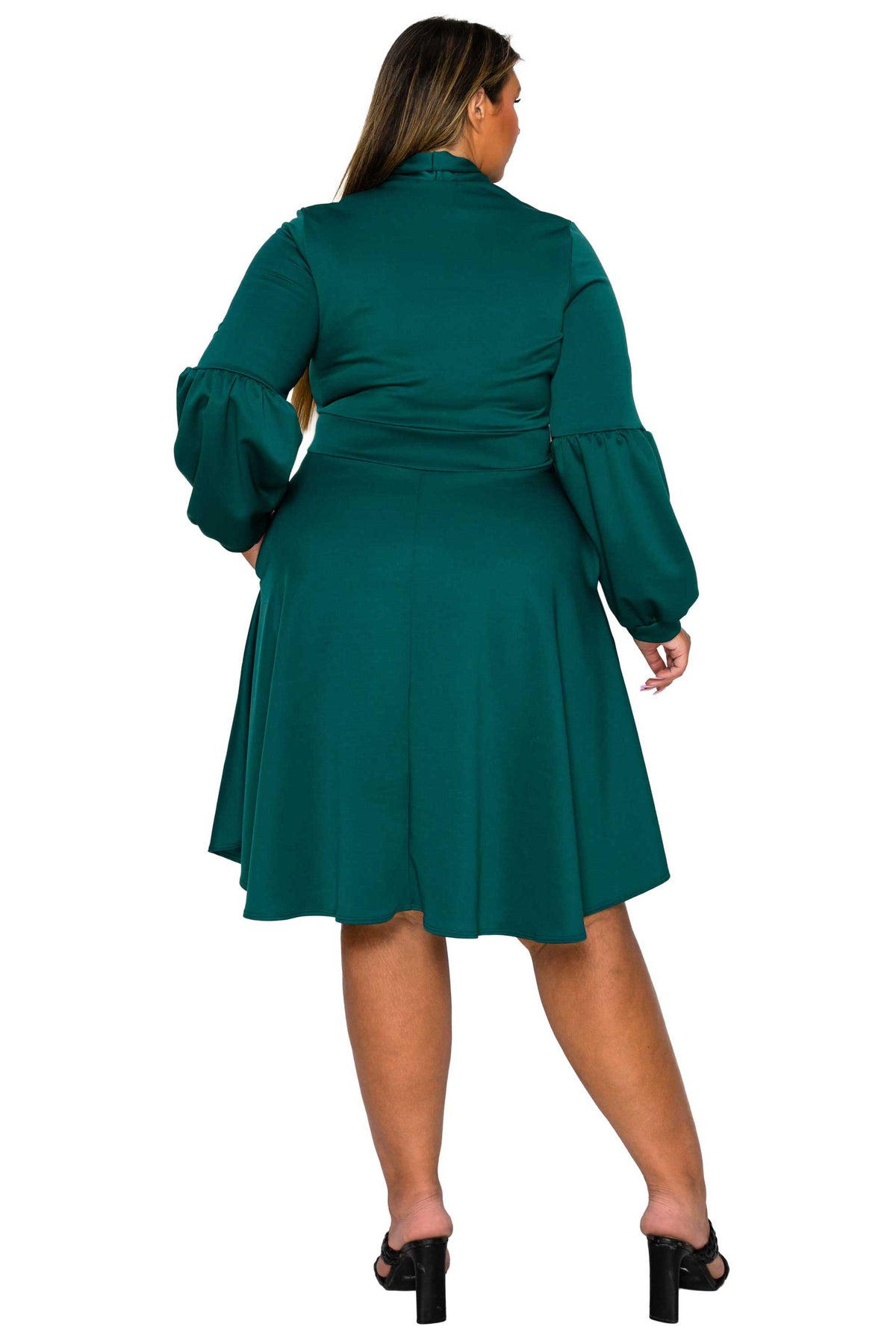 A woman shown from the back wearing a dark teal green midi dress with long balloon sleeves and a flared skirt, paired with black mule heels, against a plain white background.