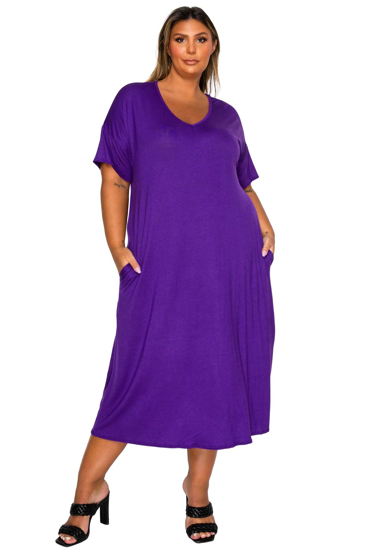 A woman modeling a purple short-sleeve maxi dress with side pockets, paired with black heeled sandals, against a plain white background.