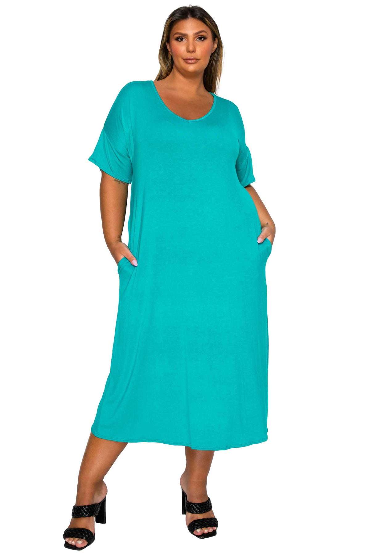 A woman modeling a short-sleeve, scoop-neck maxi dress in a vibrant turquoise color, featuring side pockets and black heeled sandals, set against a plain white background.