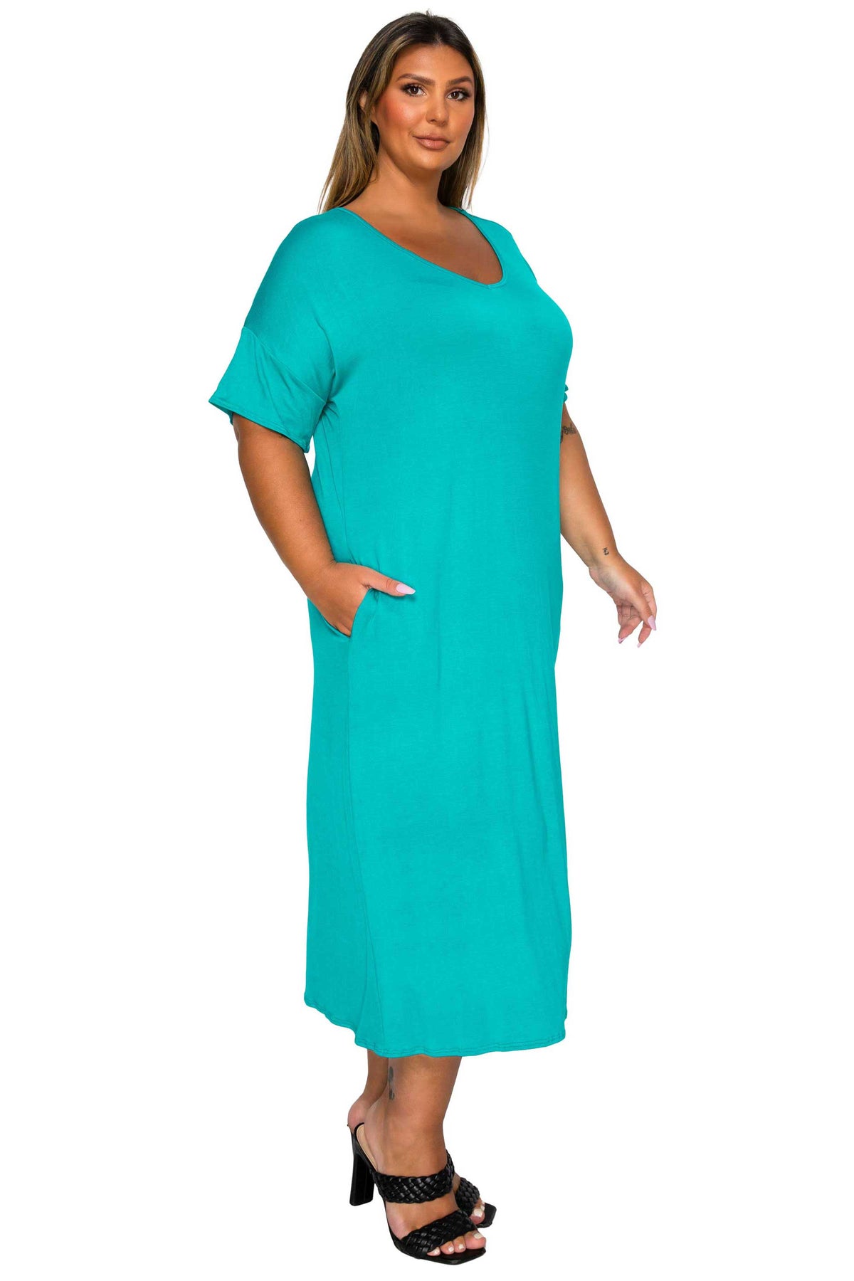 A woman modeling a short-sleeve, scoop-neck midi dress in a vibrant turquoise color, paired with black high-heeled sandals, set against a plain white background.