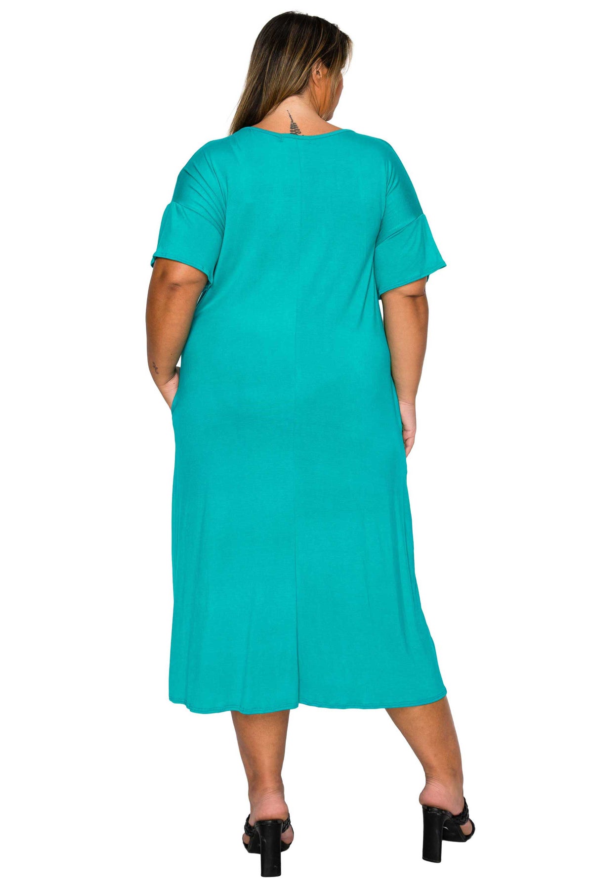 A woman viewed from the back wearing a short-sleeve turquoise maxi dress with side pockets and black heeled sandals, against a plain white background.