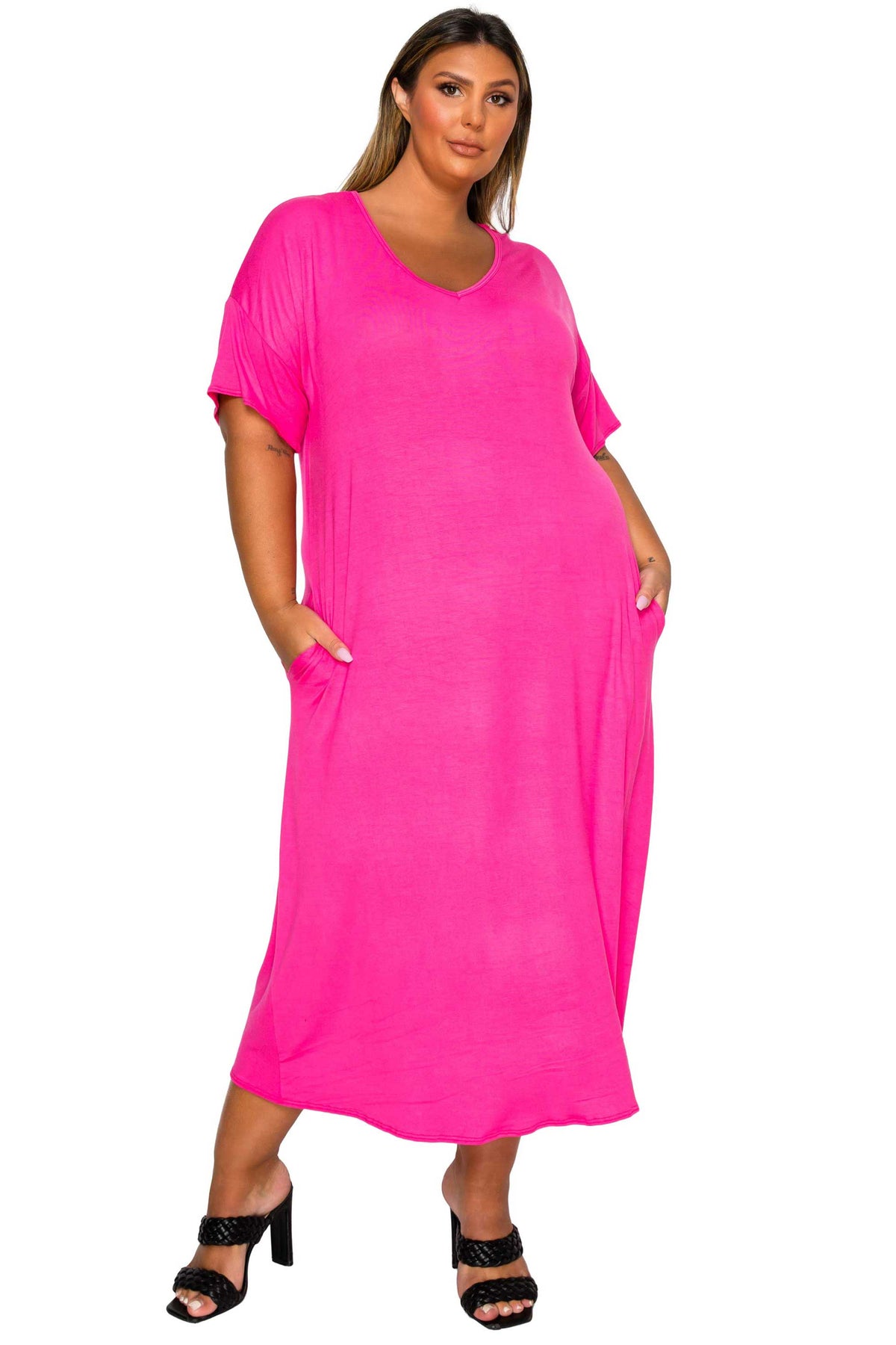 A woman modeling a bright pink short-sleeve maxi dress with side pockets, paired with black heeled sandals, against a plain white background.