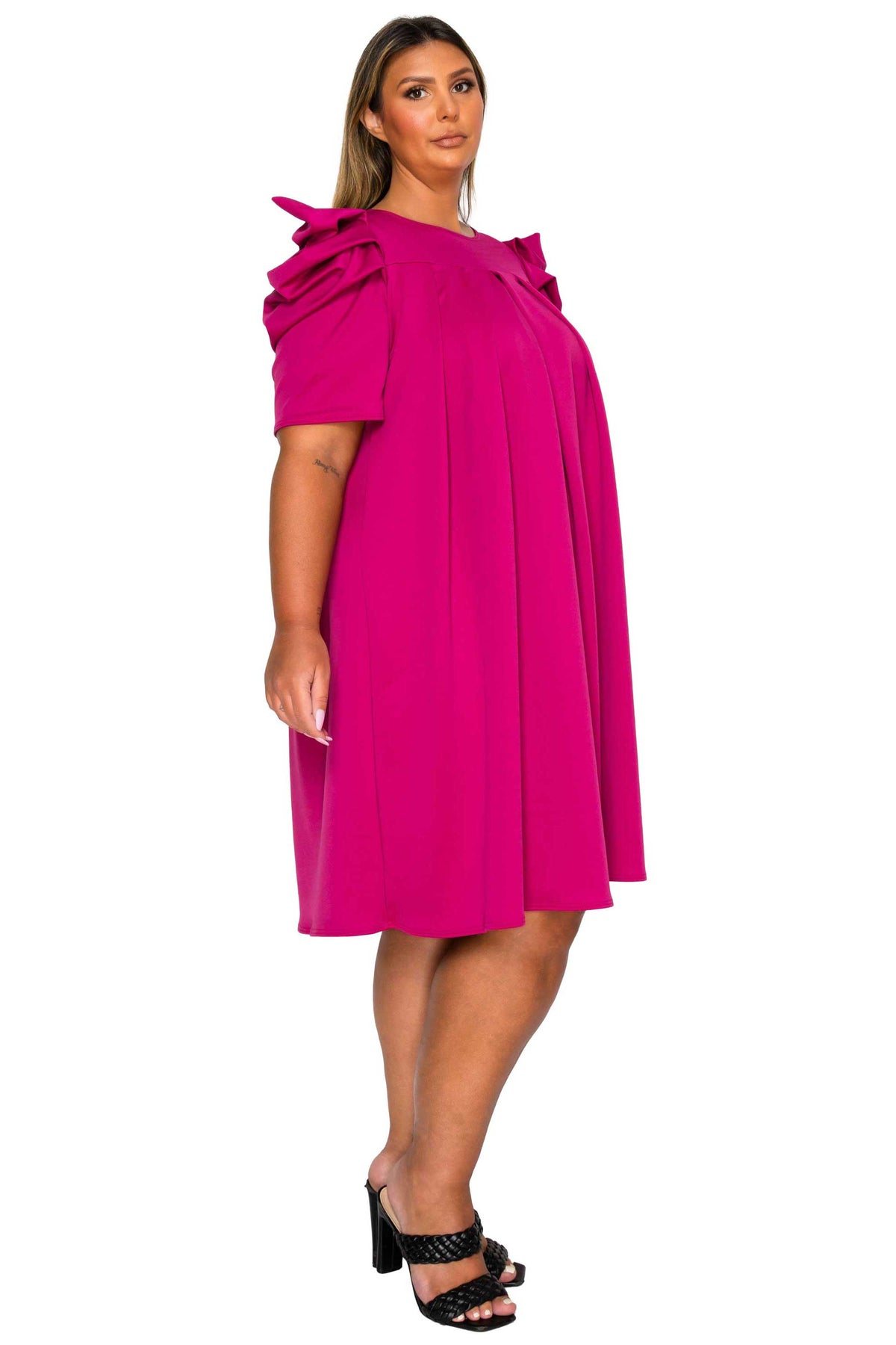 A woman modeling a bright fuchsia pink dress with a ruffled shoulder detail, photographed against a solid white background.