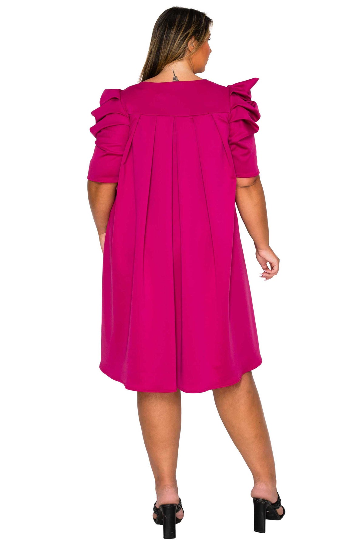 A woman viewed from the back wearing a bright fuchsia pink dress with ruffled short sleeves and a gathered waist, paired with black heeled sandals against a plain white background.