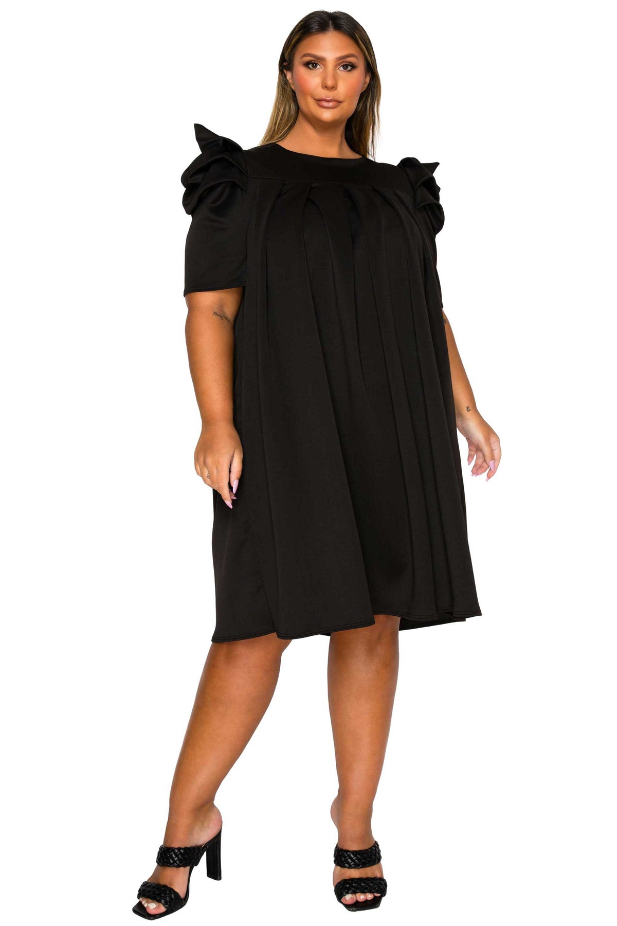 A woman modeling a black short-sleeve dress with dramatic ruffled shoulder details and a gathered neckline, paired with black strappy high-heeled sandals against a plain white background.