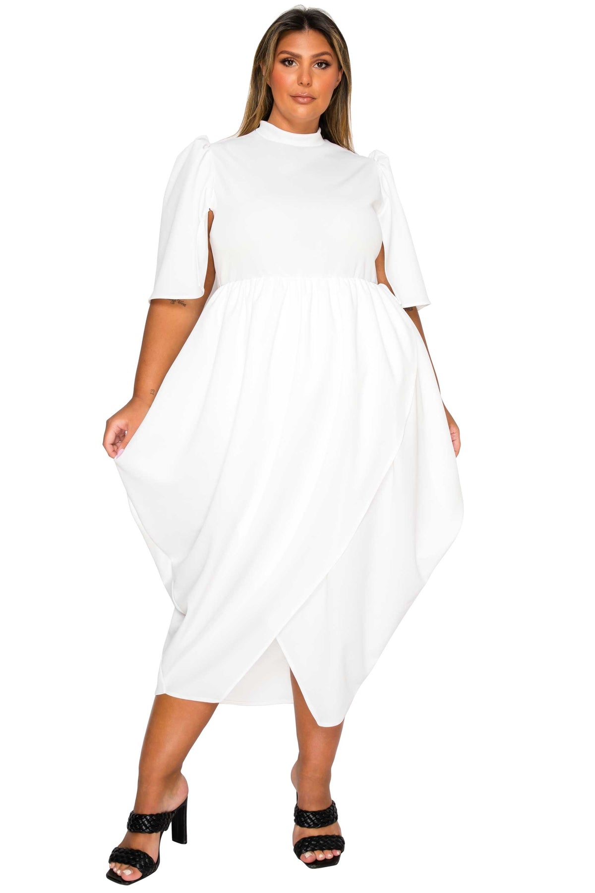 A woman modeling a white midi dress with puff sleeves, side cutouts, and an asymmetrical draped hem, paired with black heeled sandals against a plain white background.