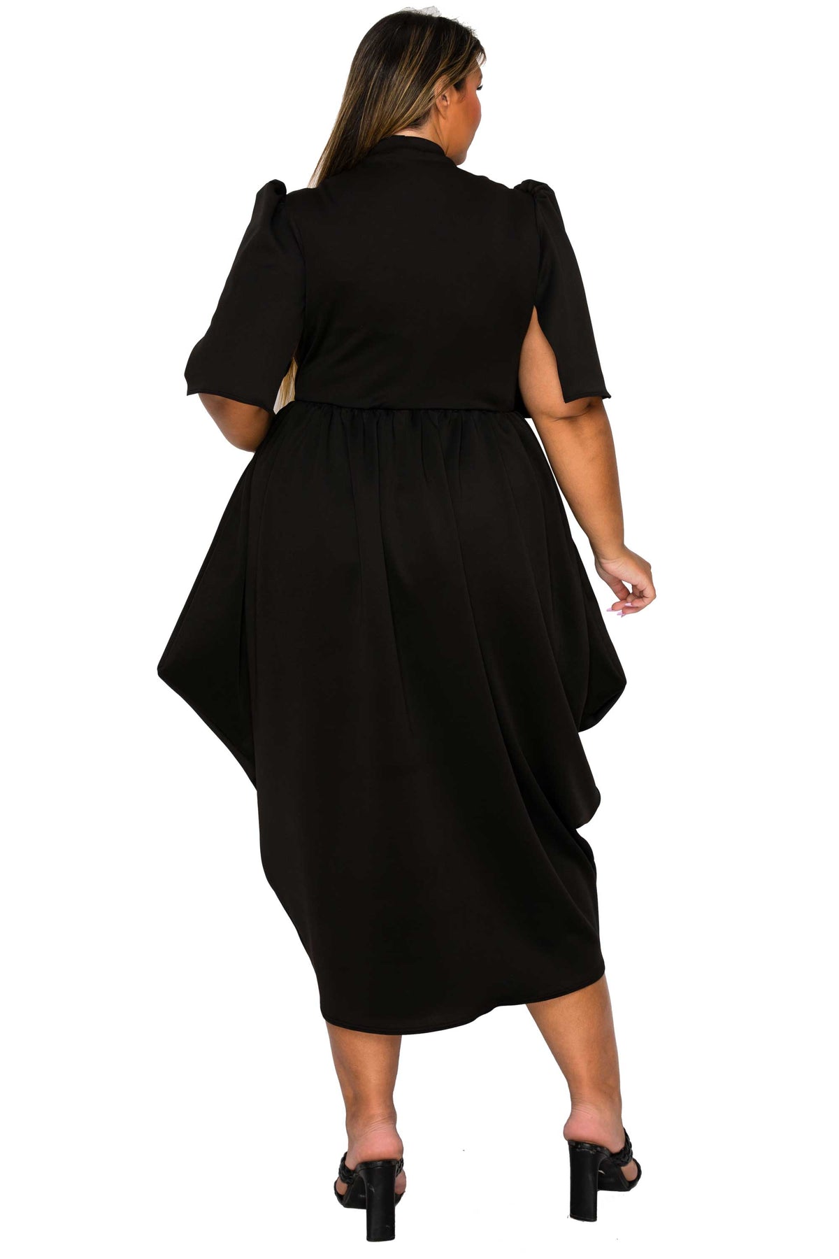 A woman shown from the back wearing a black midi dress with short puff sleeves and a draped, asymmetrical hem, paired with black heeled sandals against a plain white background.
