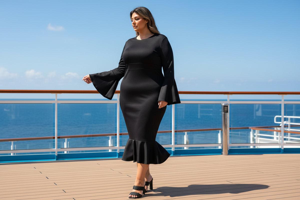 A woman modeling a black long-sleeve midi dress with flared bell sleeves and a ruffled hem, paired with black strappy heels, against a plain white background.