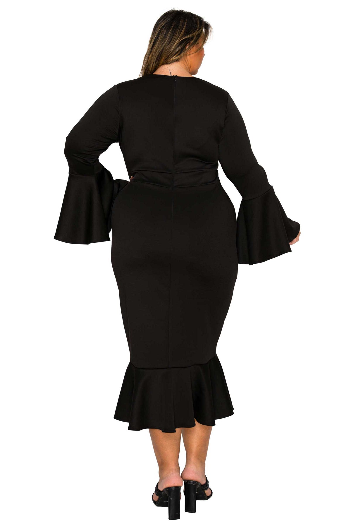 A woman viewed from the back wearing a black long-sleeve midi dress with flared bell sleeves, a fitted waist, and a ruffled hem, paired with black heeled sandals against a plain white background.