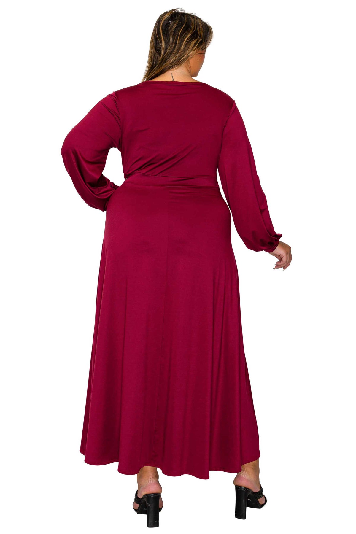 A woman viewed from the back wearing a long-sleeve maxi dress in a deep burgundy or maroon shade, paired with black high-heeled sandals, against a plain white background.