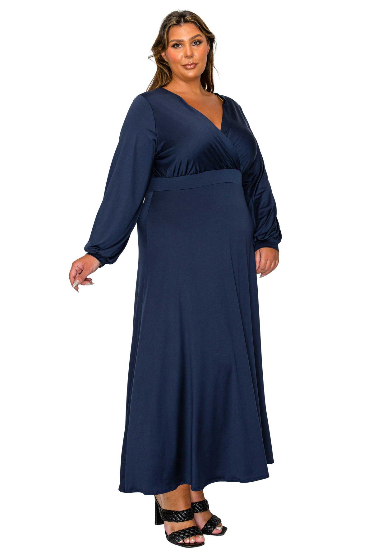 A woman modeling a navy blue long-sleeve maxi dress with a wrap-style V-neck bodice and a fitted waistband, shown against a plain white background.