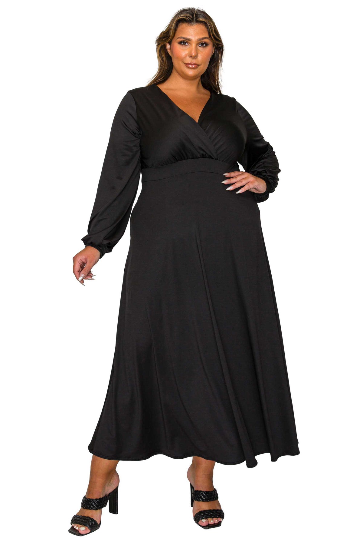 A woman modeling a long-sleeve black maxi dress with a wrap-style V-neck bodice and a flowing skirt, paired with black heeled sandals, against a plain white background.