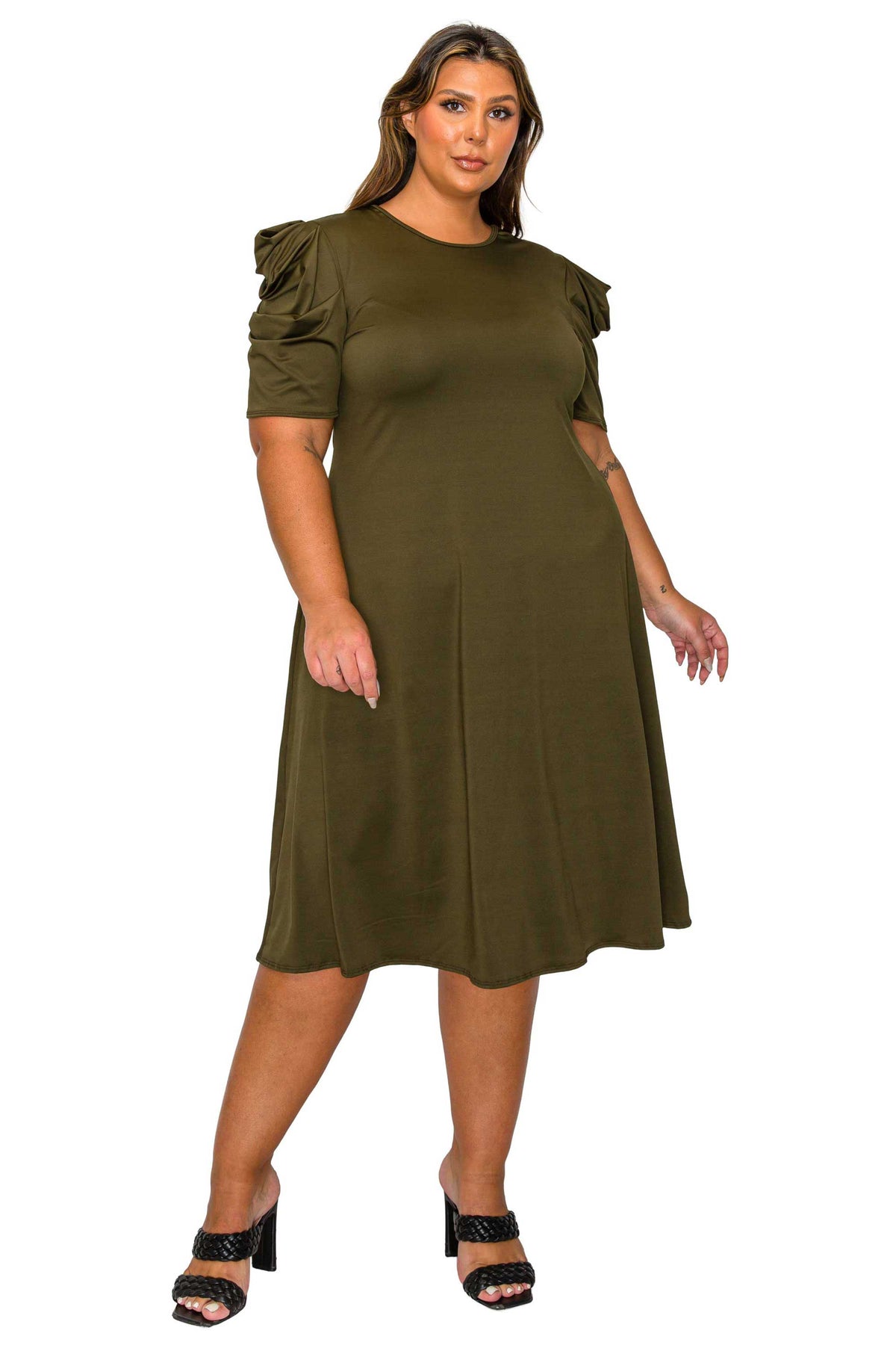 A woman modeling a knee-length olive green dress with short puff sleeves and black heeled sandals against a plain white background.