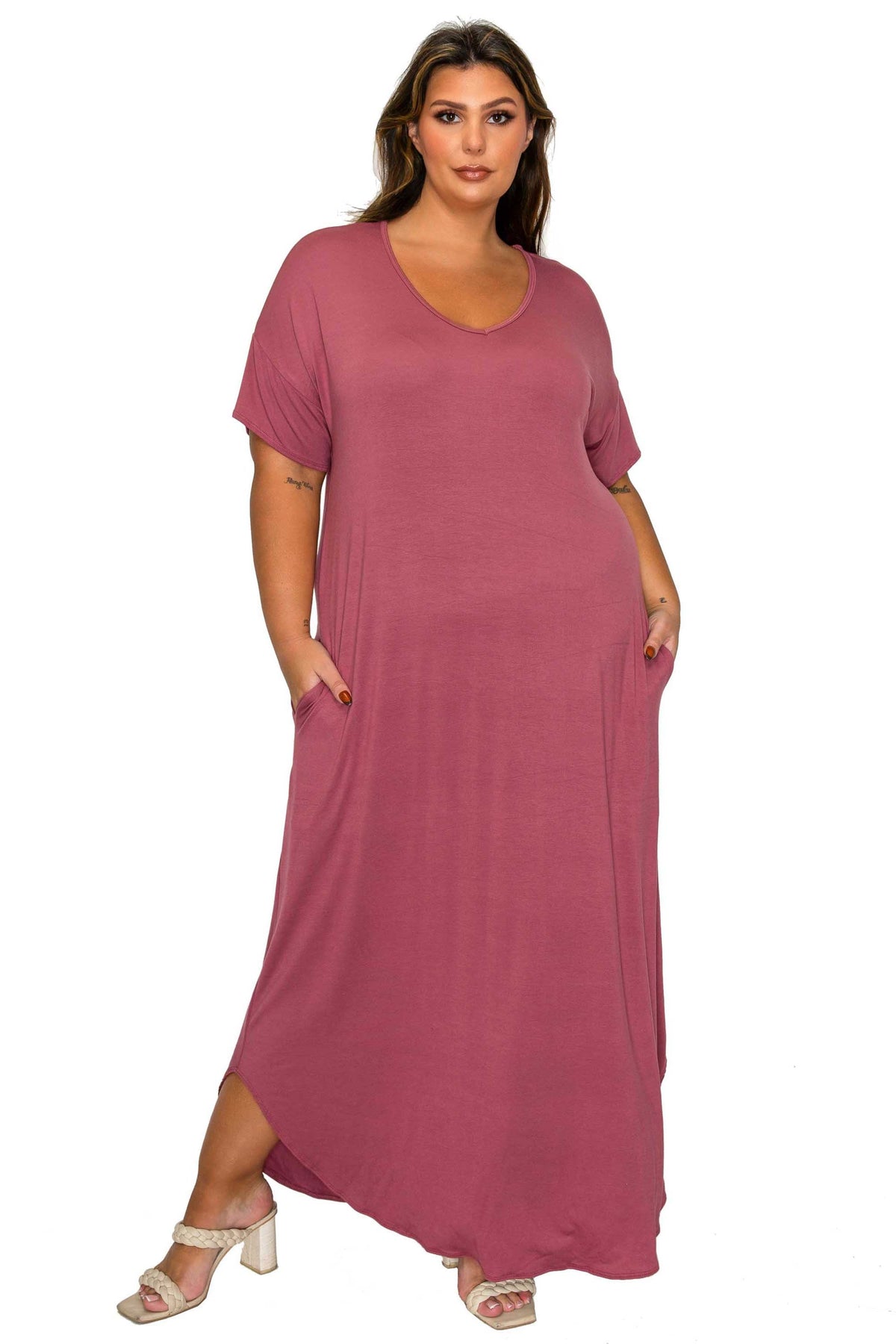 A woman modeling a dusty rose pink short-sleeve maxi dress with side pockets, paired with white heeled sandals, against a plain white background.