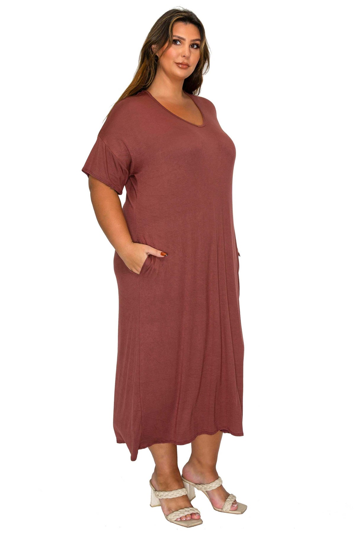 A woman modeling a loose, short-sleeve maxi dress in a dusty rose color, featuring side pockets and a V-neckline, paired with white heeled sandals against a plain white background.