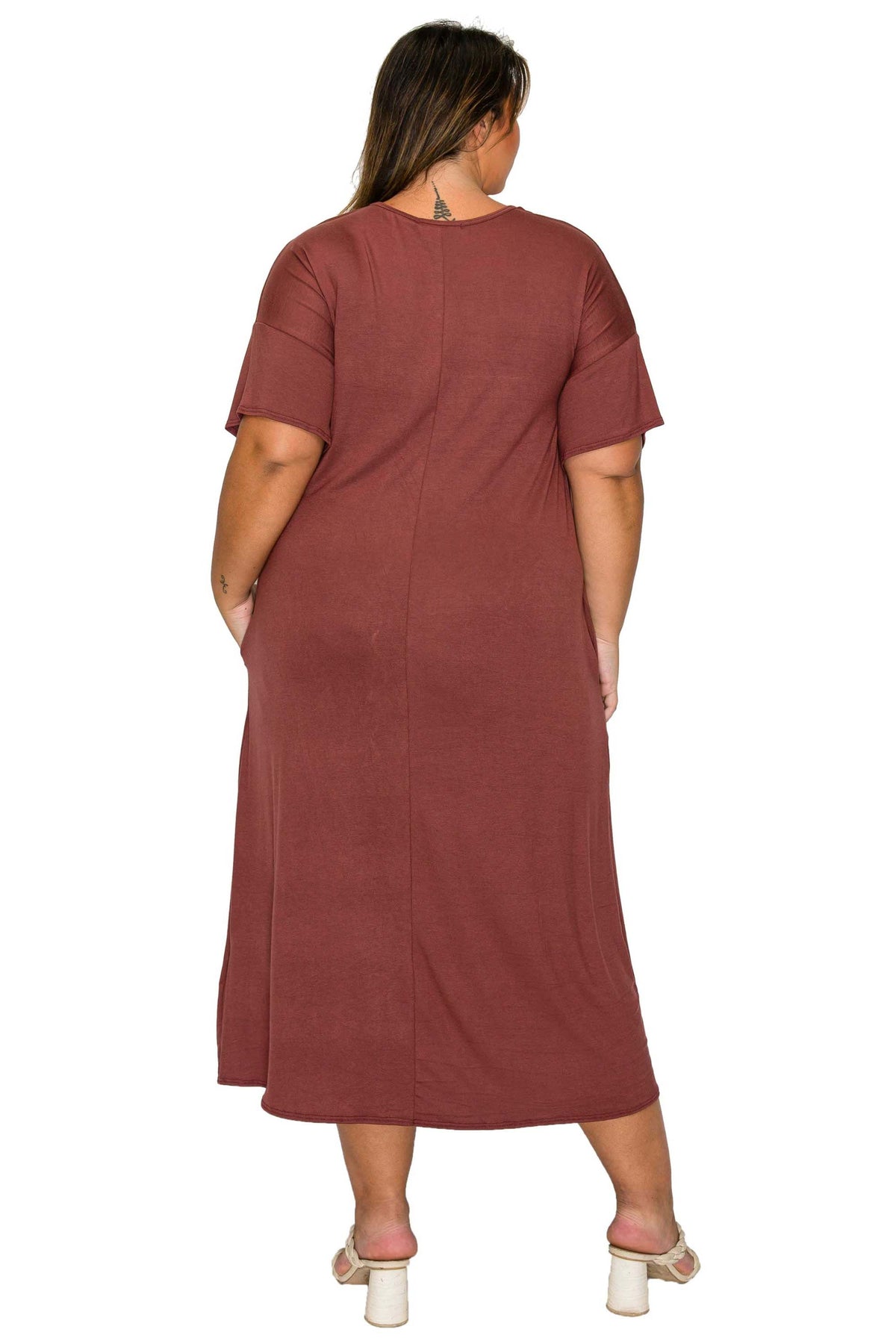 A woman shown from the back wearing a short-sleeve, knee-length dusty rose maxi dress with side pockets, paired with white heeled sandals, against a plain white background.
