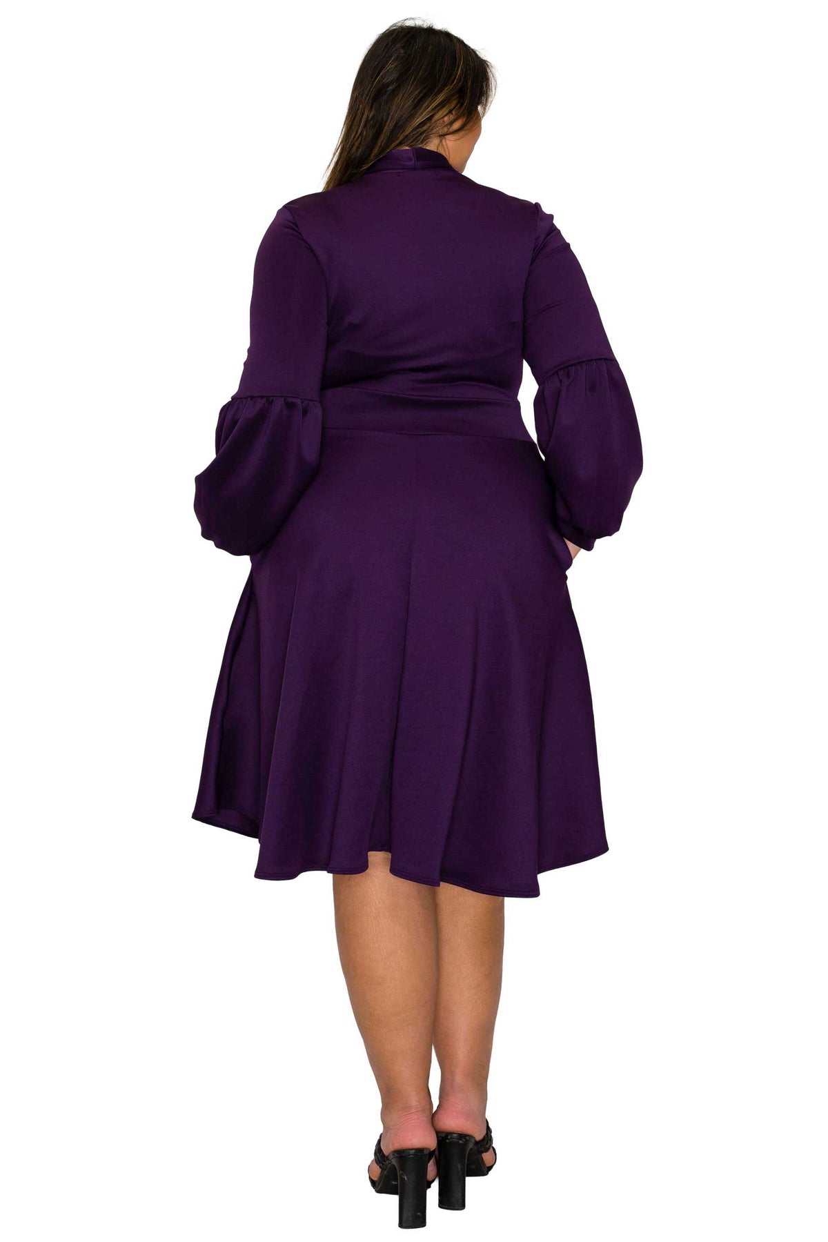 A woman viewed from the back wearing a knee-length purple dress with long balloon sleeves and black high-heeled sandals against a plain white background.