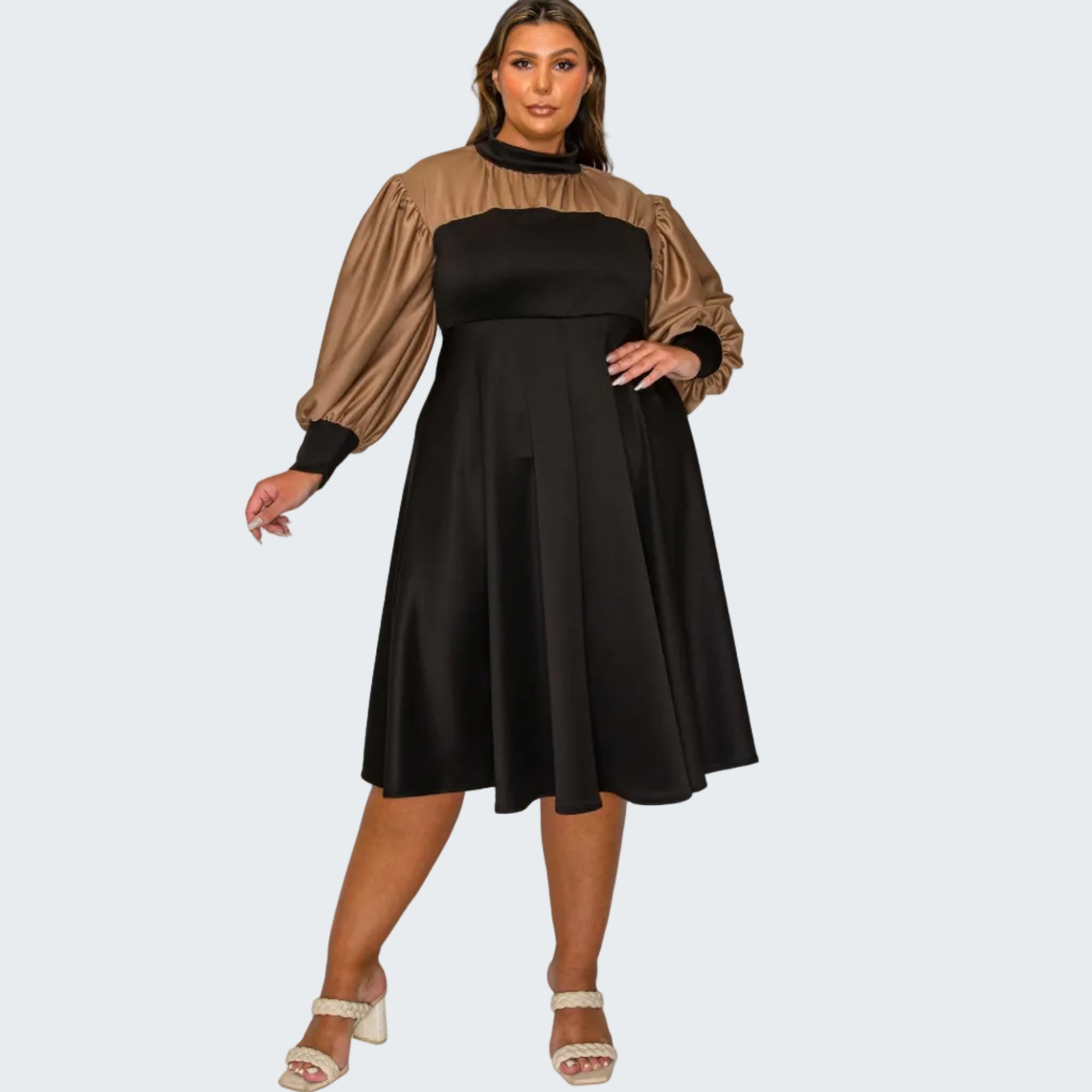 A woman modeling a black midi dress with a brown yoke and puffed long sleeves, paired with white heeled sandals, against a plain white background.