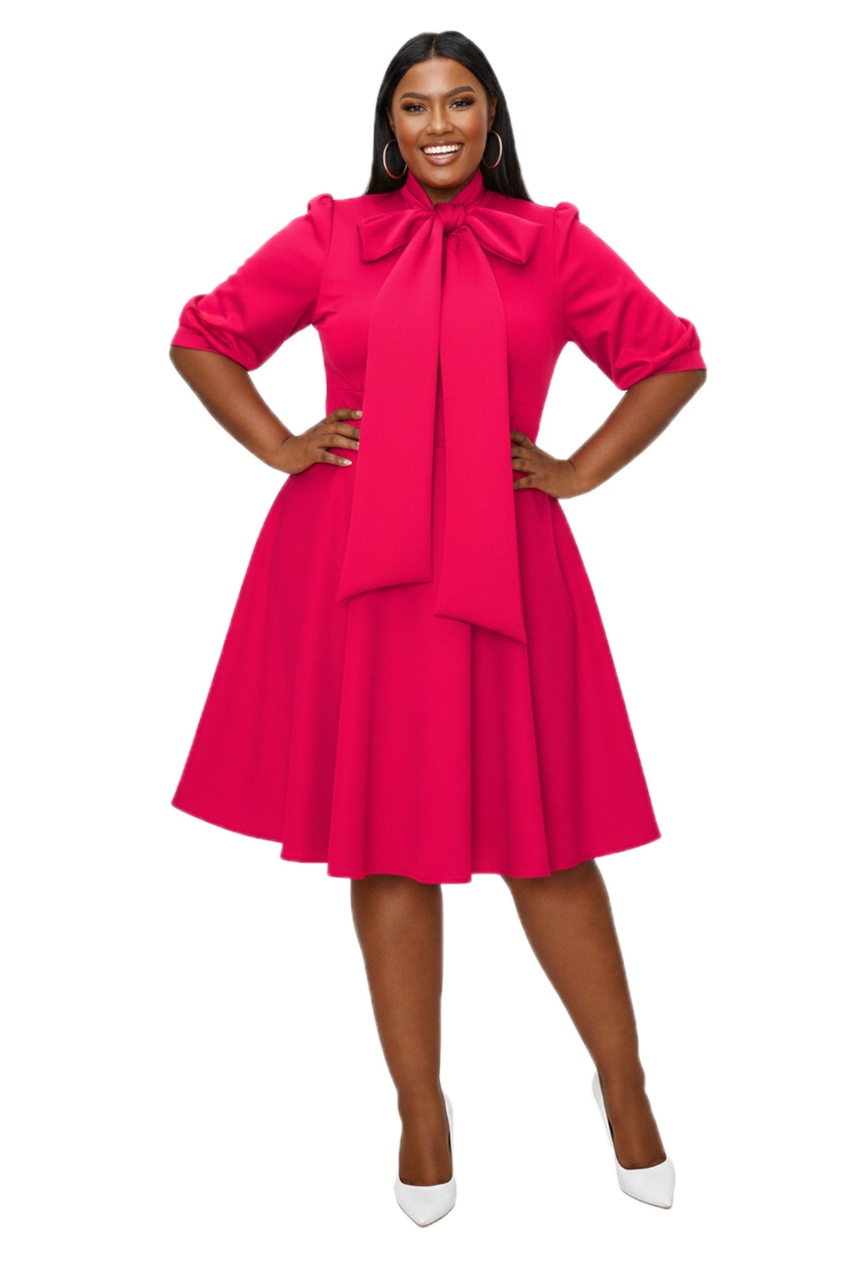 A woman modeling a bright pink midi dress with a large bow at the collar, ruffled three-quarter sleeves, and a flared skirt, paired with white pointed-toe heels against a plain white background.