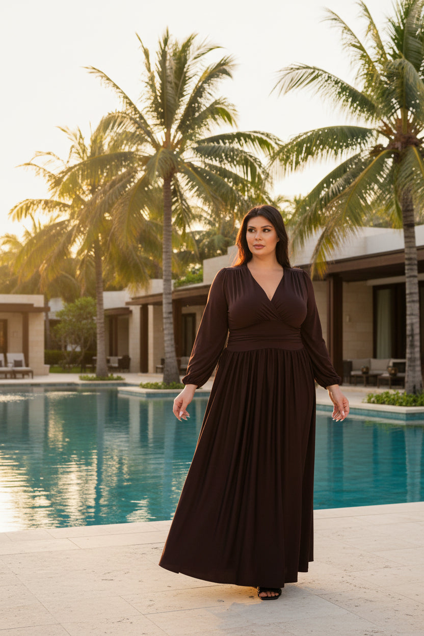A woman modeling a long-sleeve, dark brown wrap-style maxi dress with a pleated skirt, shown against a plain white background.