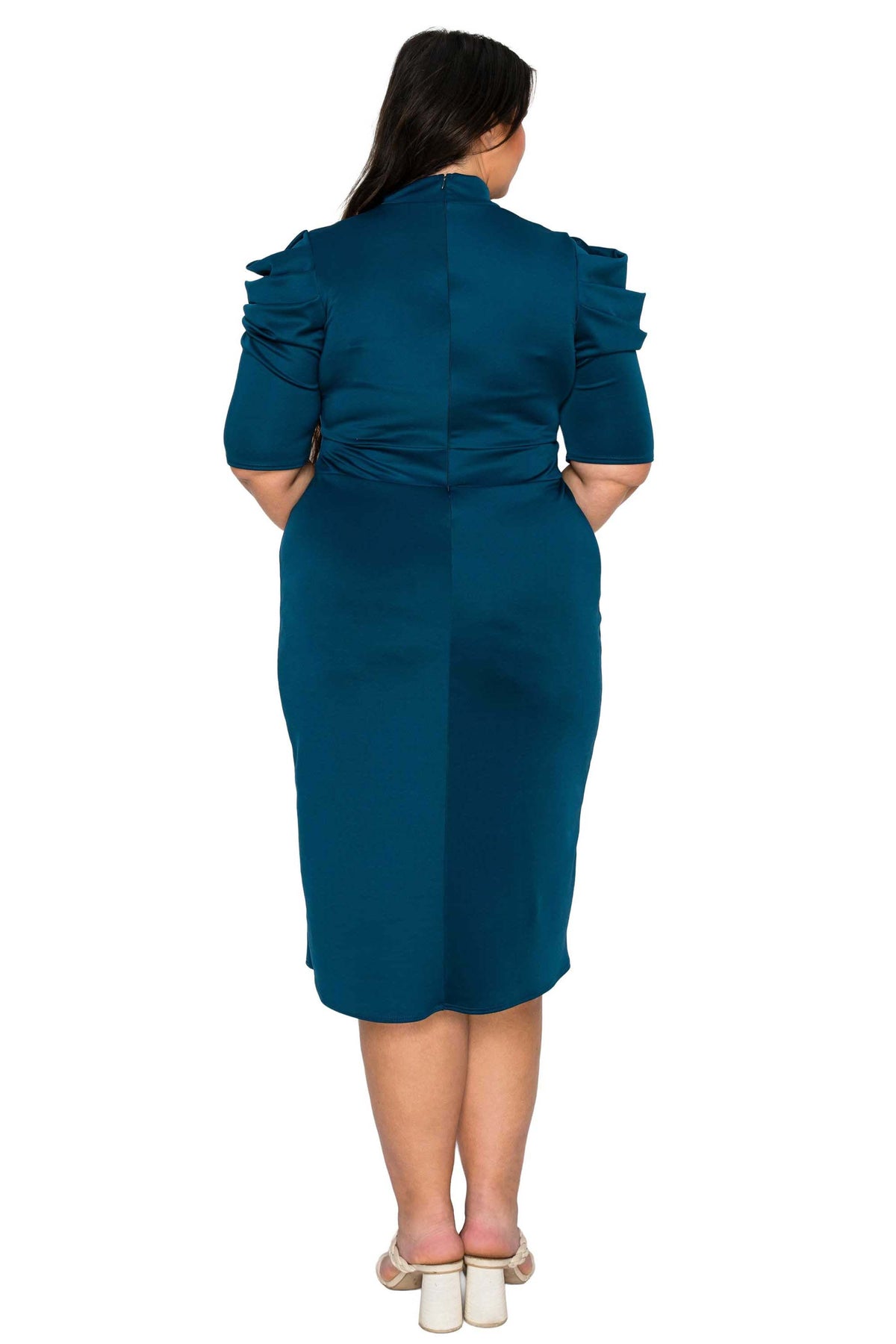 A woman viewed from the back wearing a teal knee-length dress with ruffled short sleeves and structured shoulders, paired with white block-heeled sandals, against a plain white background.
