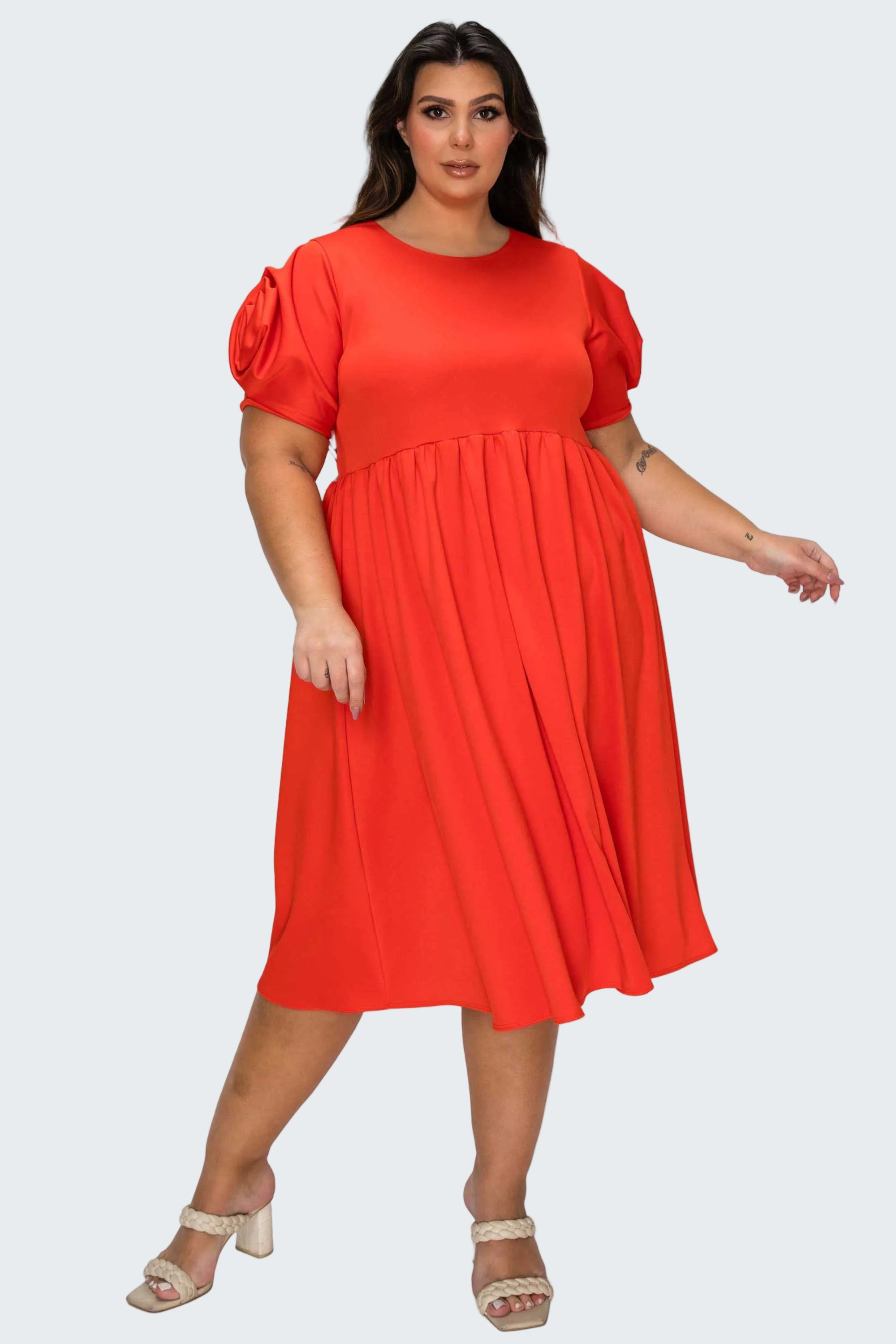 A woman modeling a bright red midi dress with short puff sleeves and a gathered waist, paired with beige heeled sandals, against a plain white background.