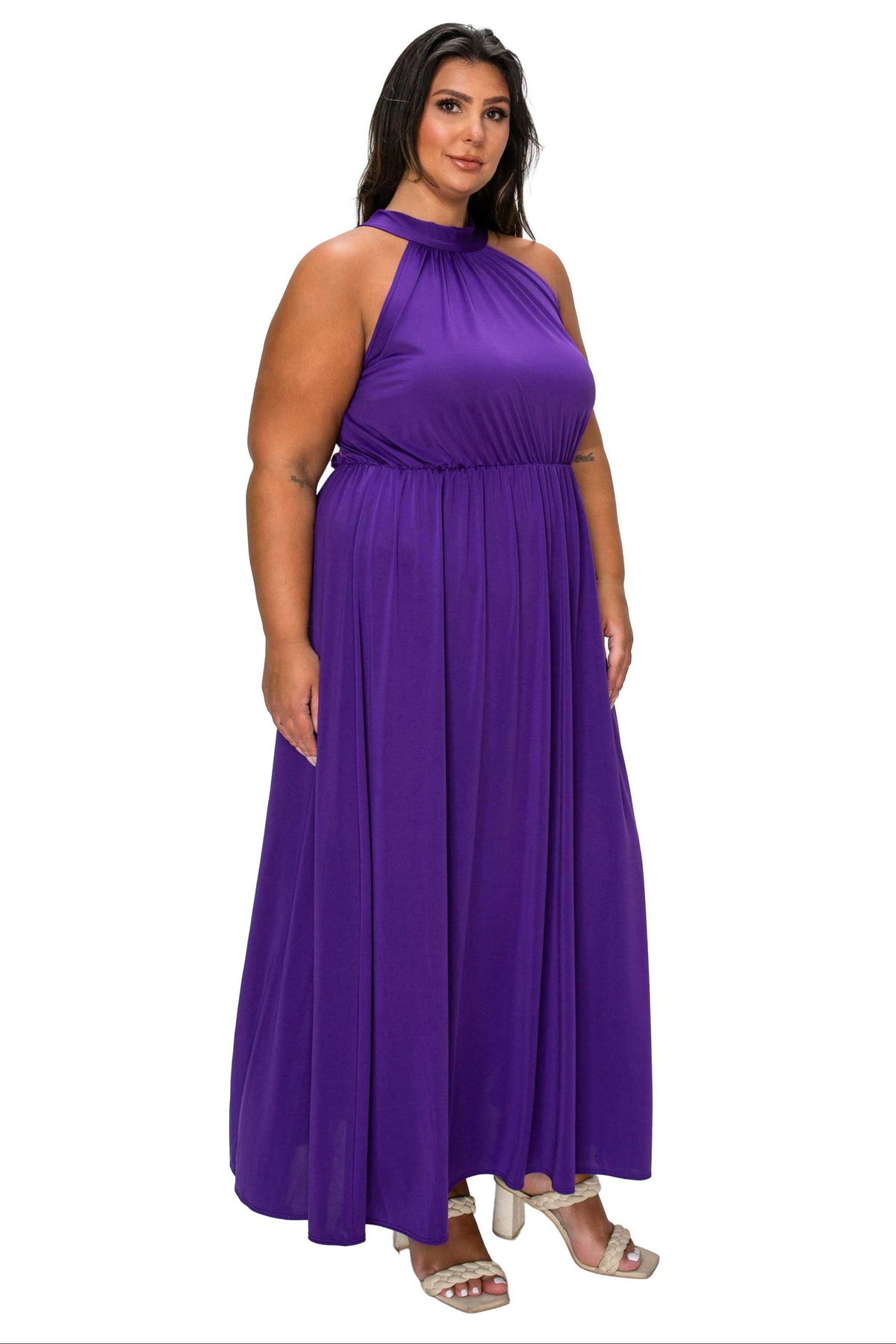 A woman modeling a sleeveless, high-neck, floor-length purple dress with a gathered waist, shown against a plain white background.