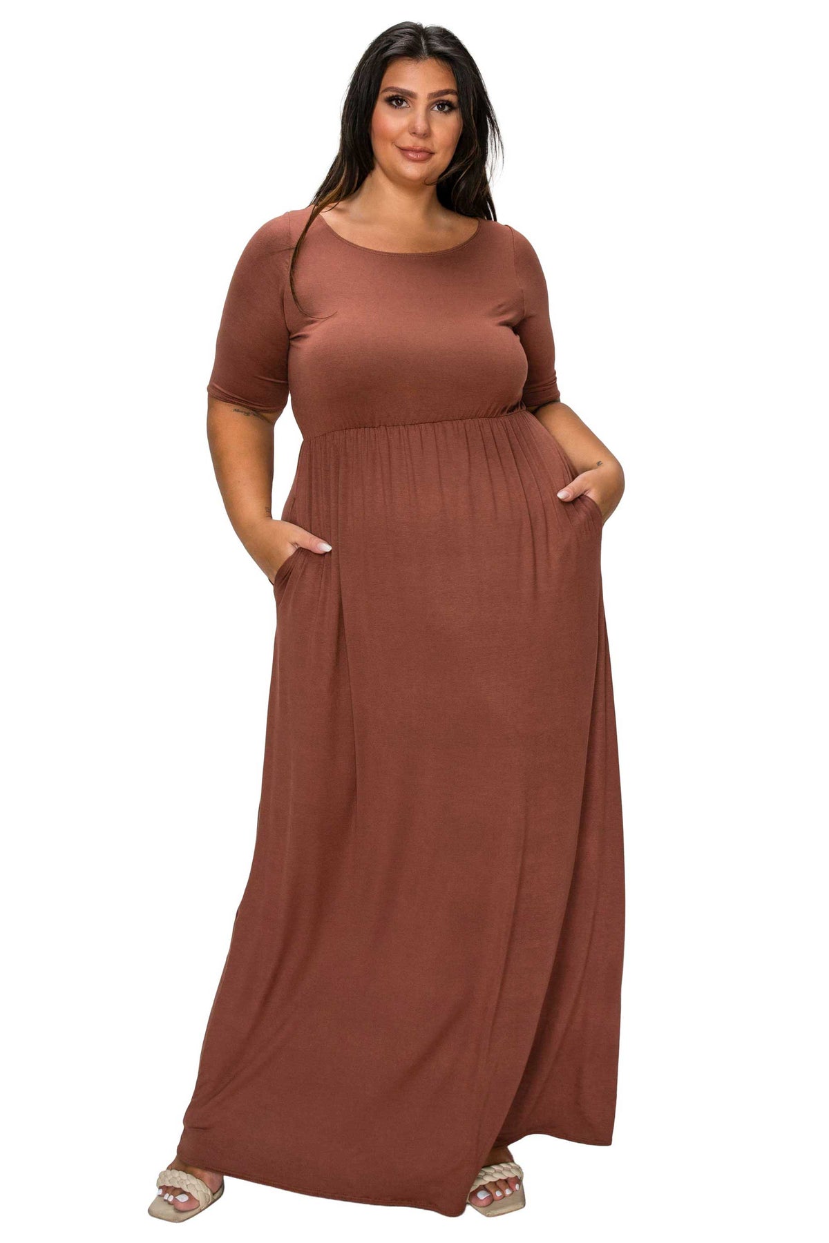A woman modeling a rust-brown, short-sleeved maxi dress with side pockets, shown against a plain white background.