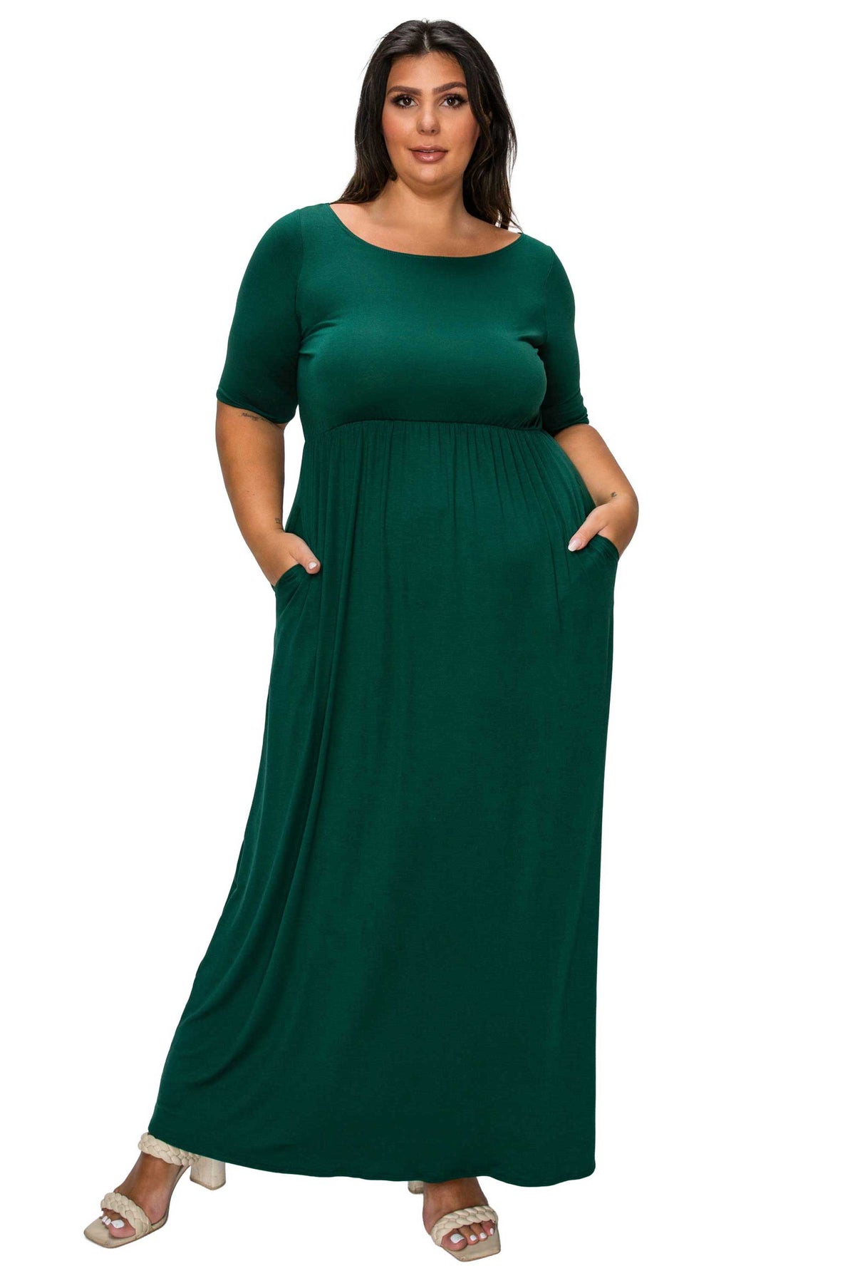 A woman modeling a dark green, short-sleeved maxi dress with side pockets, shown against a plain white background.