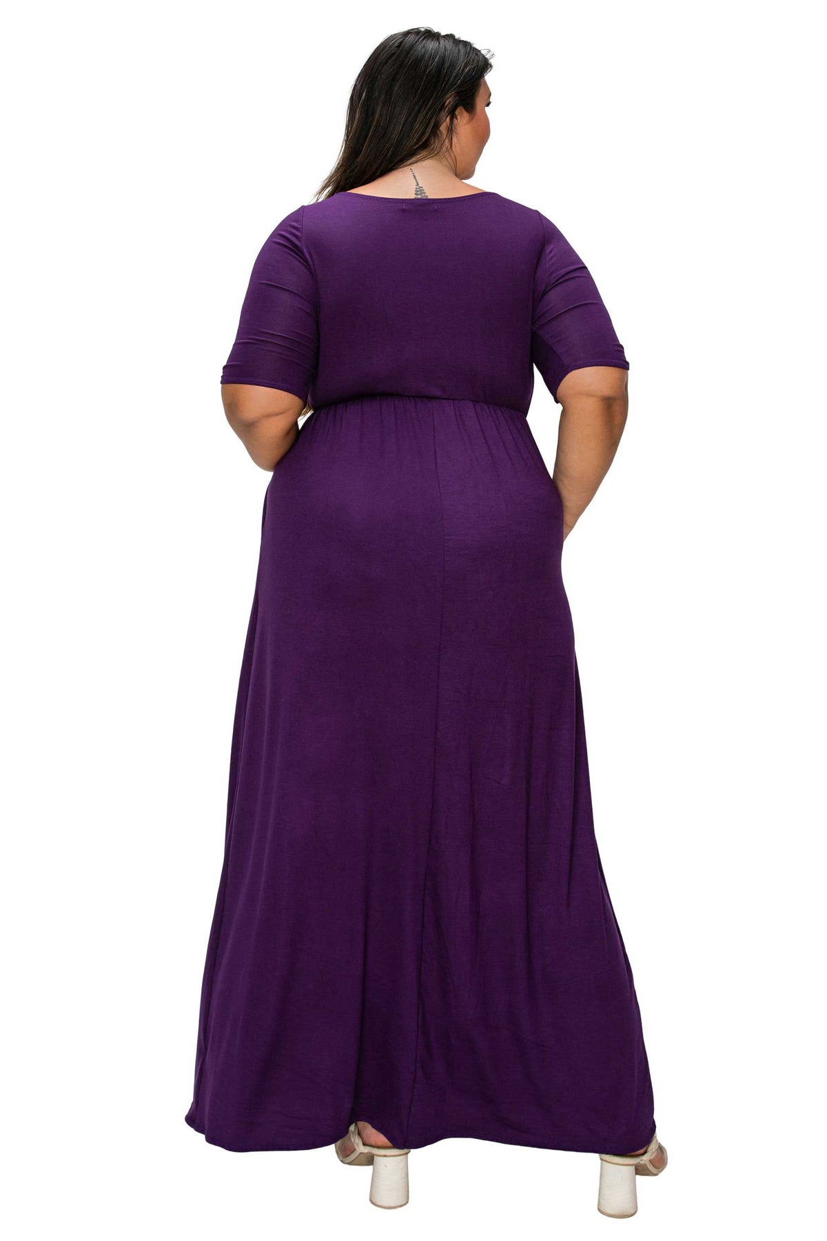 A woman viewed from the back wearing a long purple maxi dress with short sleeves and a gathered waist, standing against a plain white background.