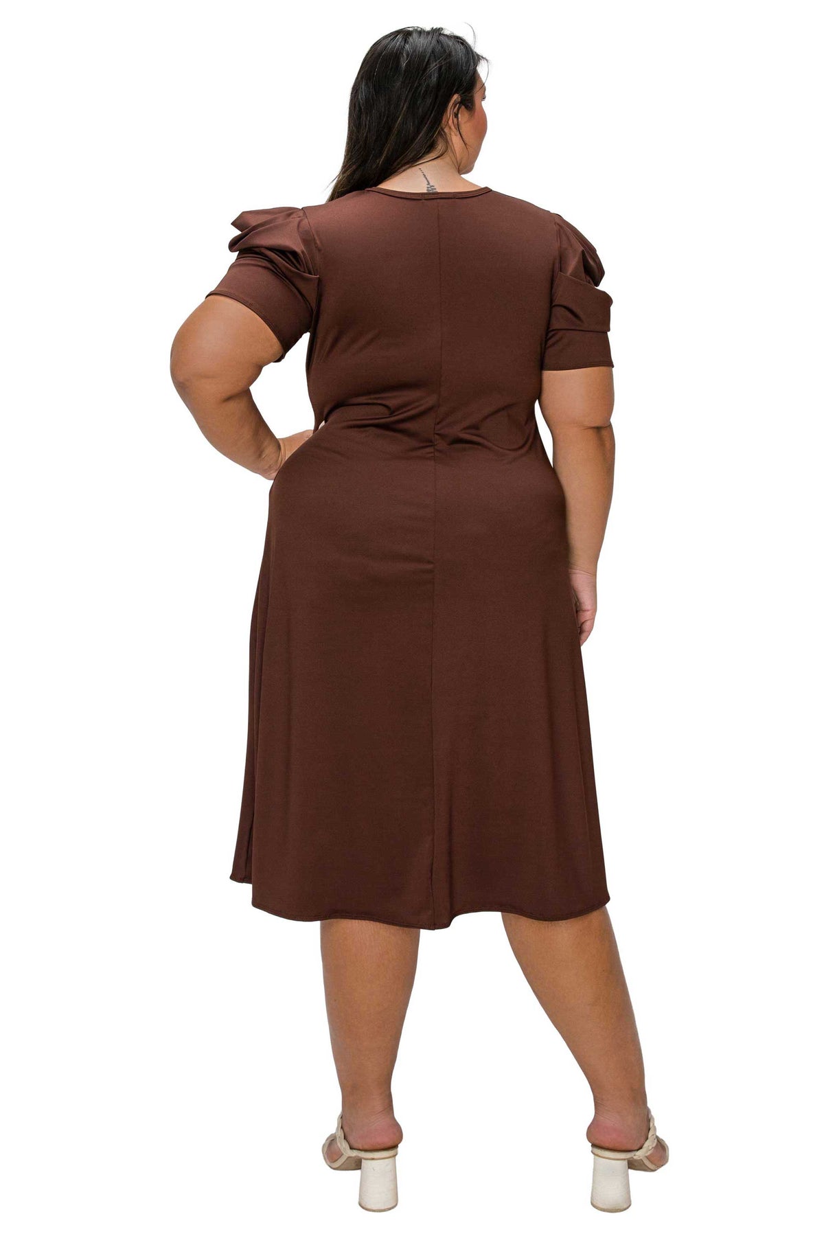 A woman shown from the back wearing a brown short-sleeve midi dress with puffed shoulders and a tie at the waist, paired with white heeled sandals, against a plain white background.
