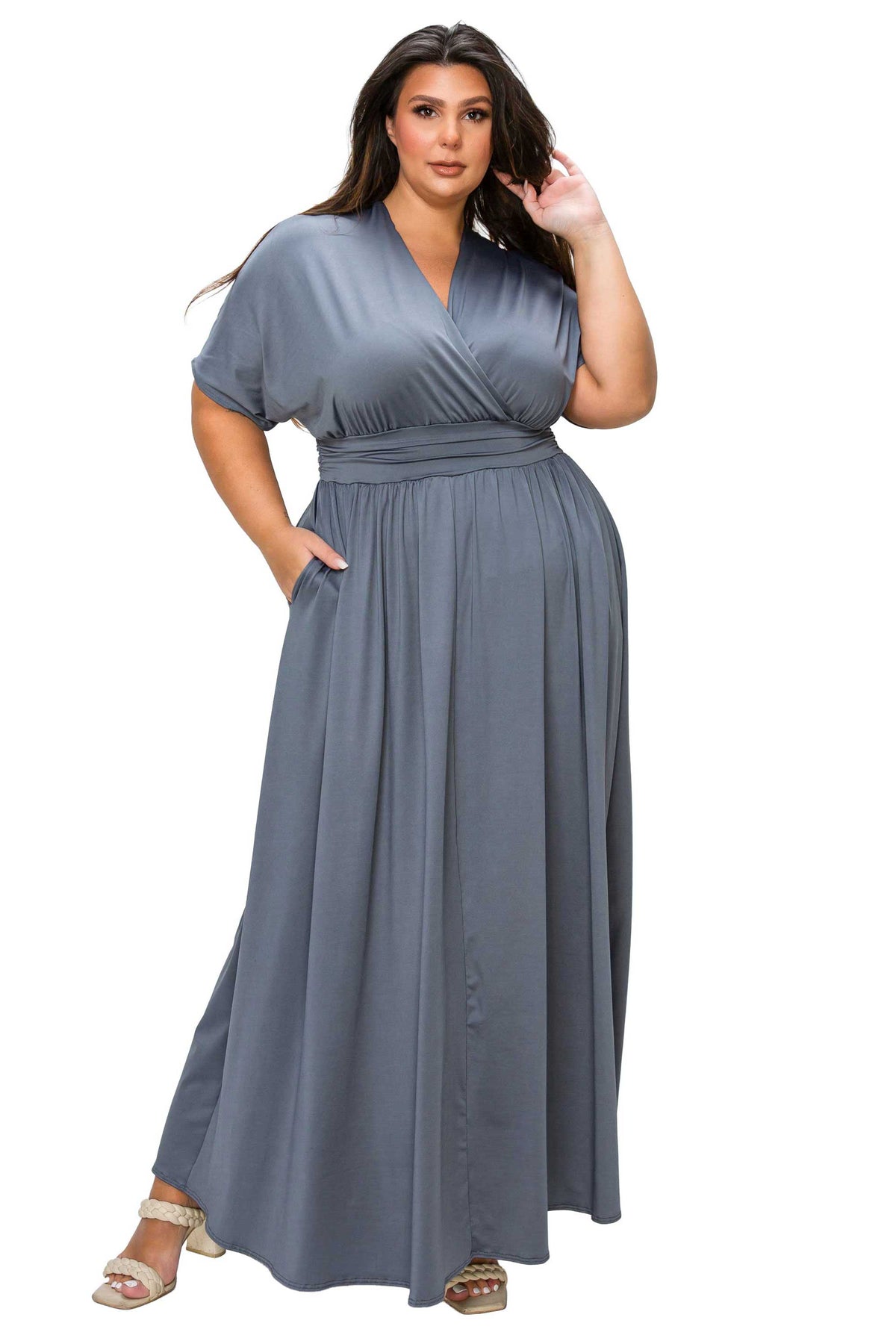 A woman modeling a slate blue-gray maxi dress with short sleeves, a V-neckline, side pockets, and a matching fabric belt at the waist, shown against a plain white background.