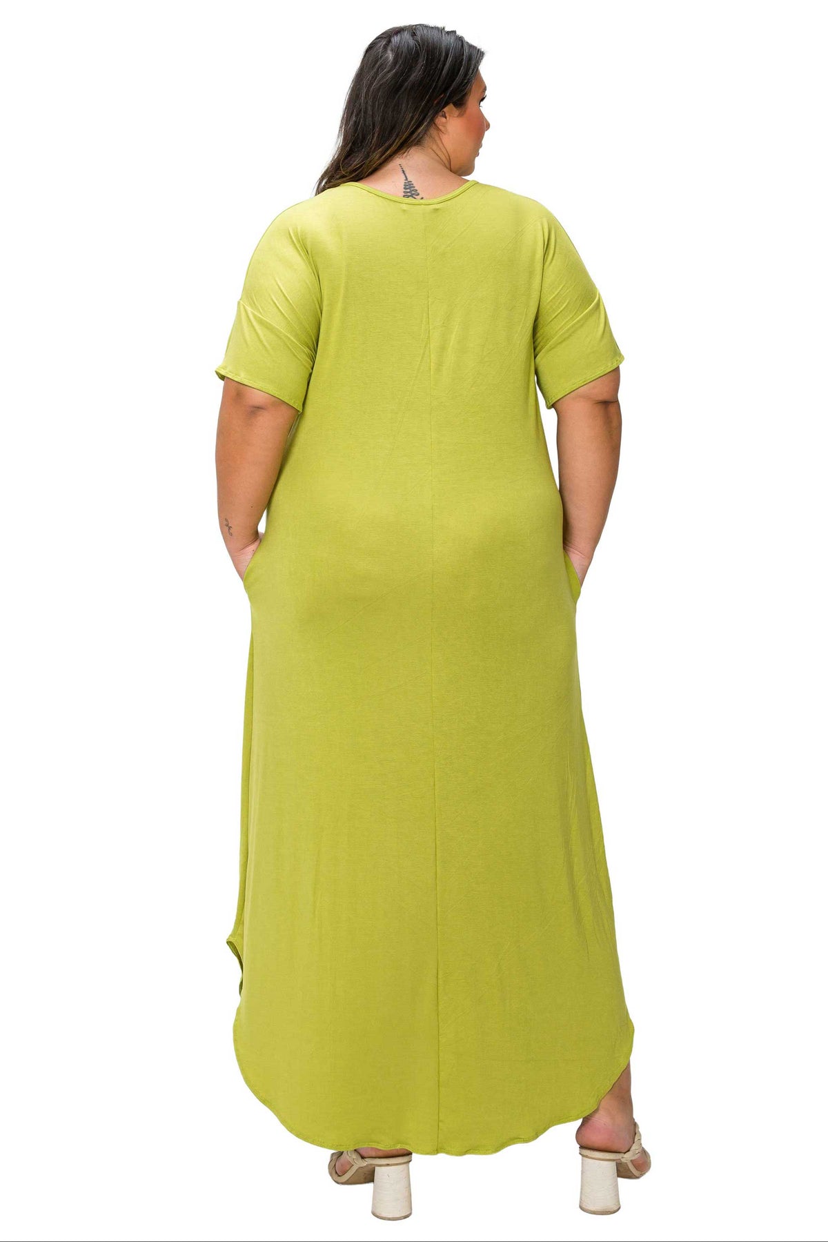 A woman viewed from the back wearing a bright lime green short-sleeve maxi dress with side pockets, paired with white block-heel sandals, against a plain white background.