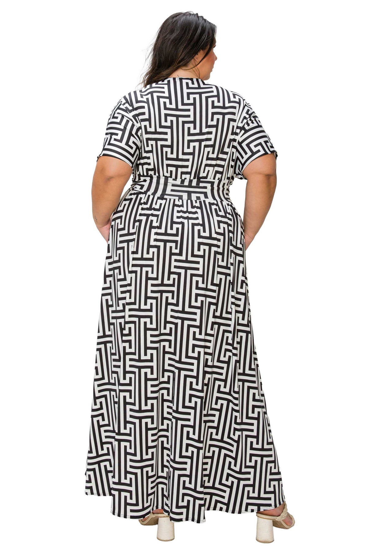 A woman viewed from the back wearing a short-sleeve maxi dress with a black and white geometric maze-like pattern and a matching tie belt at the waist, set against a plain white background.