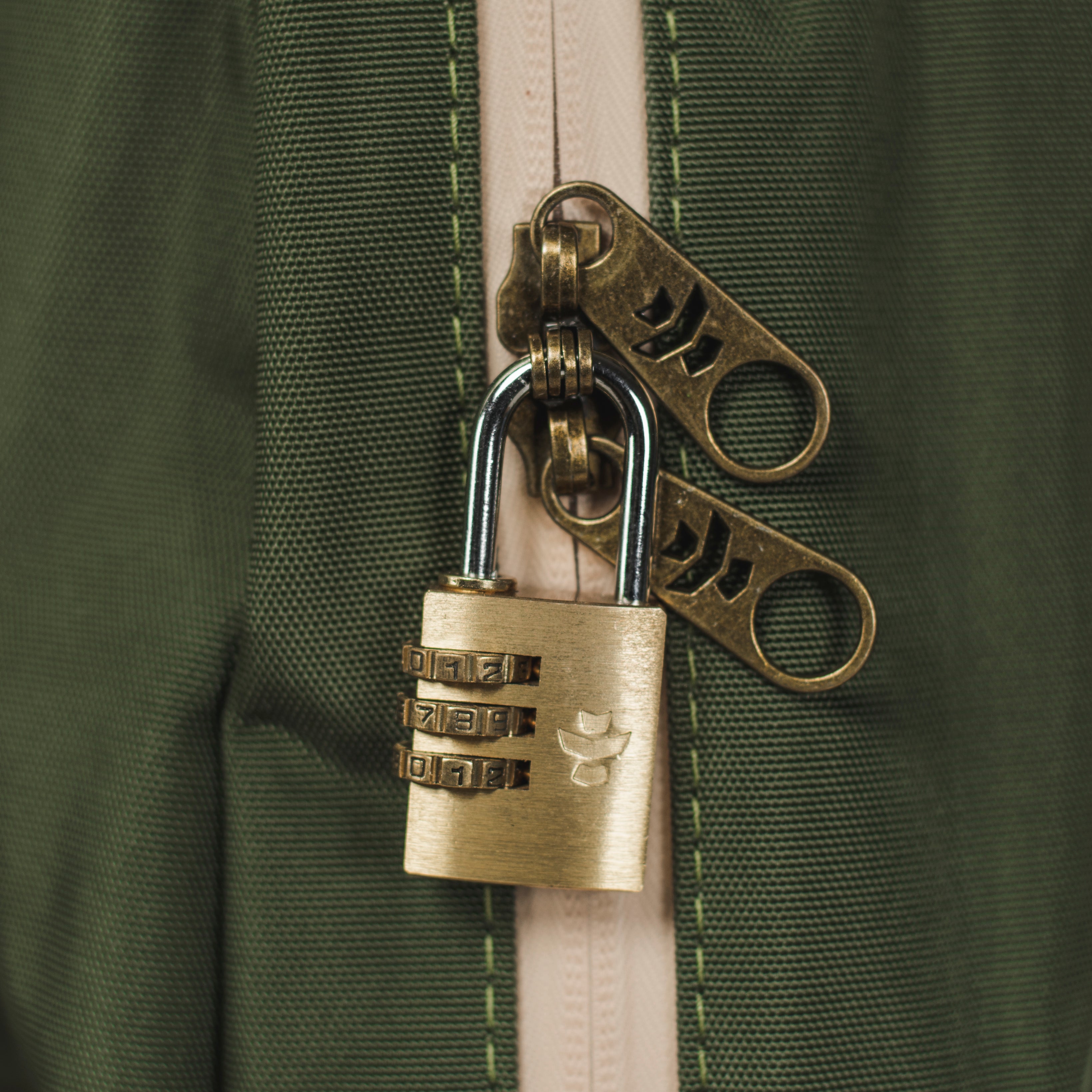 Brass combination lock attached to a green zipper on a green background