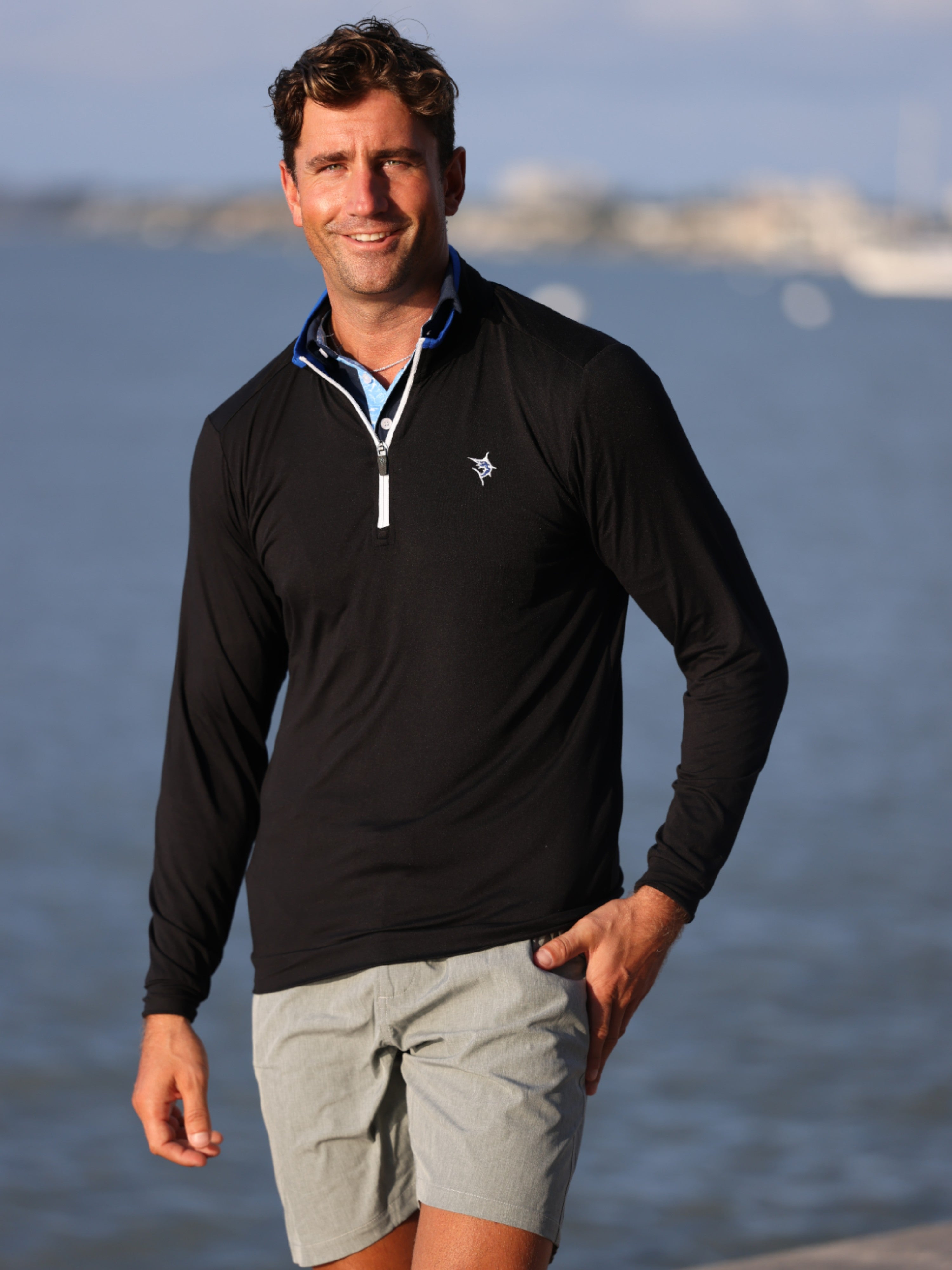 Man wearing a black long-sleeve shirt and gray shorts standing by a body of water.