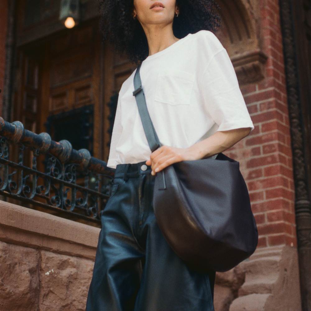 Person holding a dark blue bag against a brick wall background