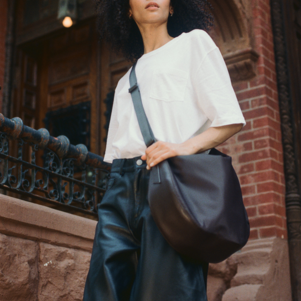 Person holding a dark blue bag against a brick wall background