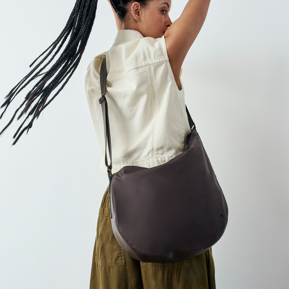 Woman carrying a dark brown shoulder bag against a plain background