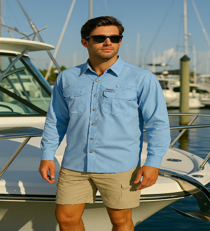 Man wearing a light blue shirt with a logo and beige shorts standing on a boat in a marina.