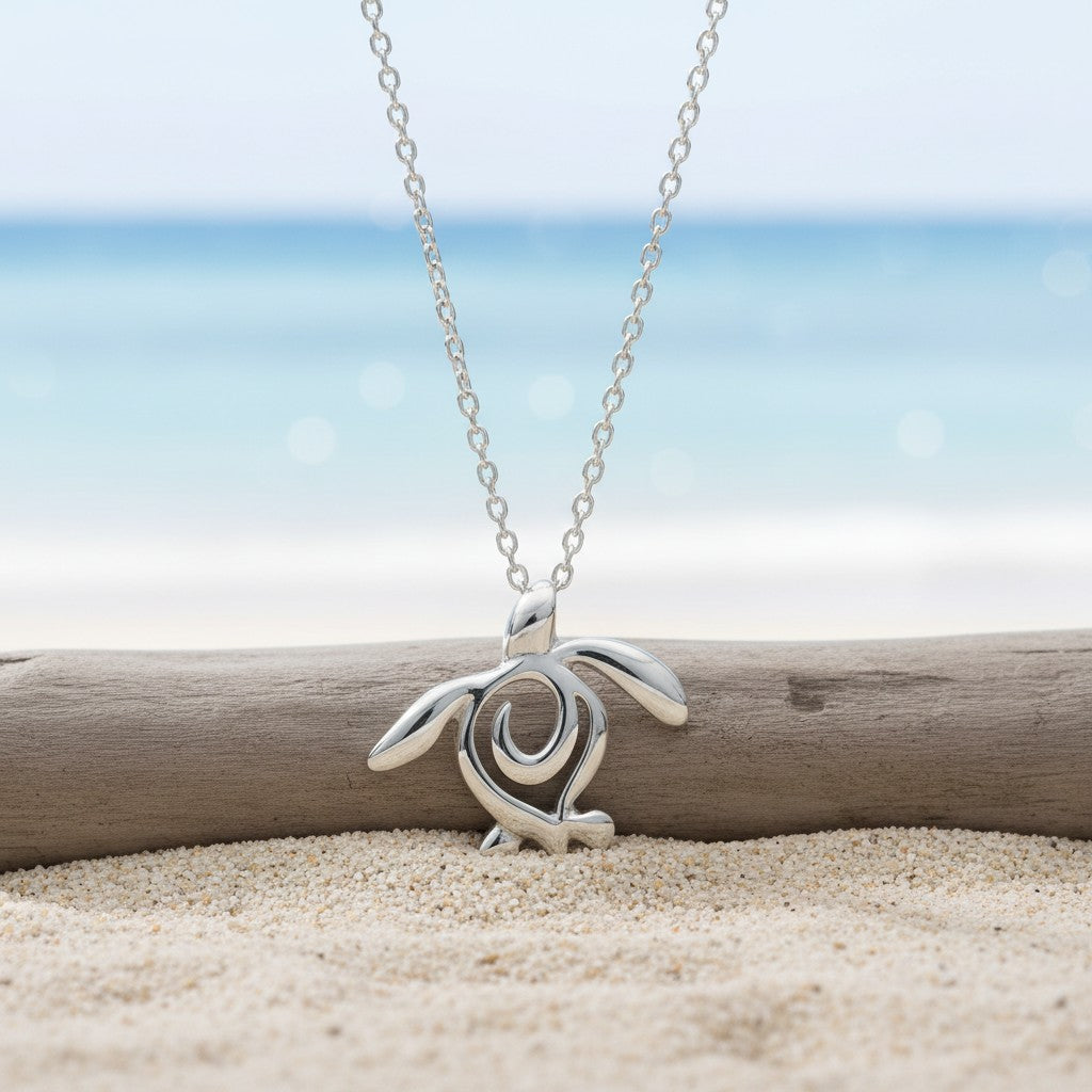 Silver turtle pendant necklace on a chain, placed on sand with a blurred beach background
