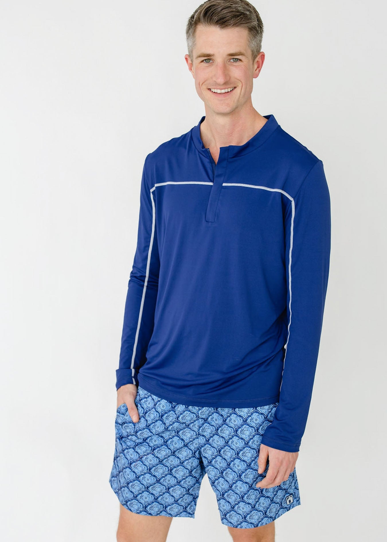 Man wearing a blue long-sleeve shirt and patterned shorts on a white background