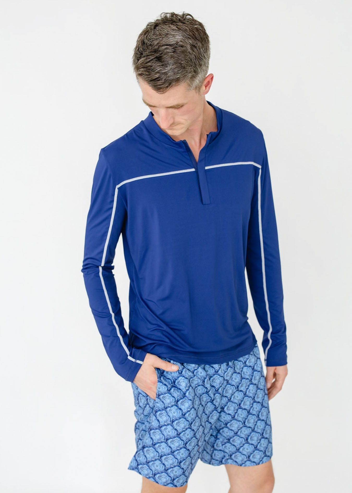 Man wearing a blue long-sleeve shirt and patterned shorts on a white background
