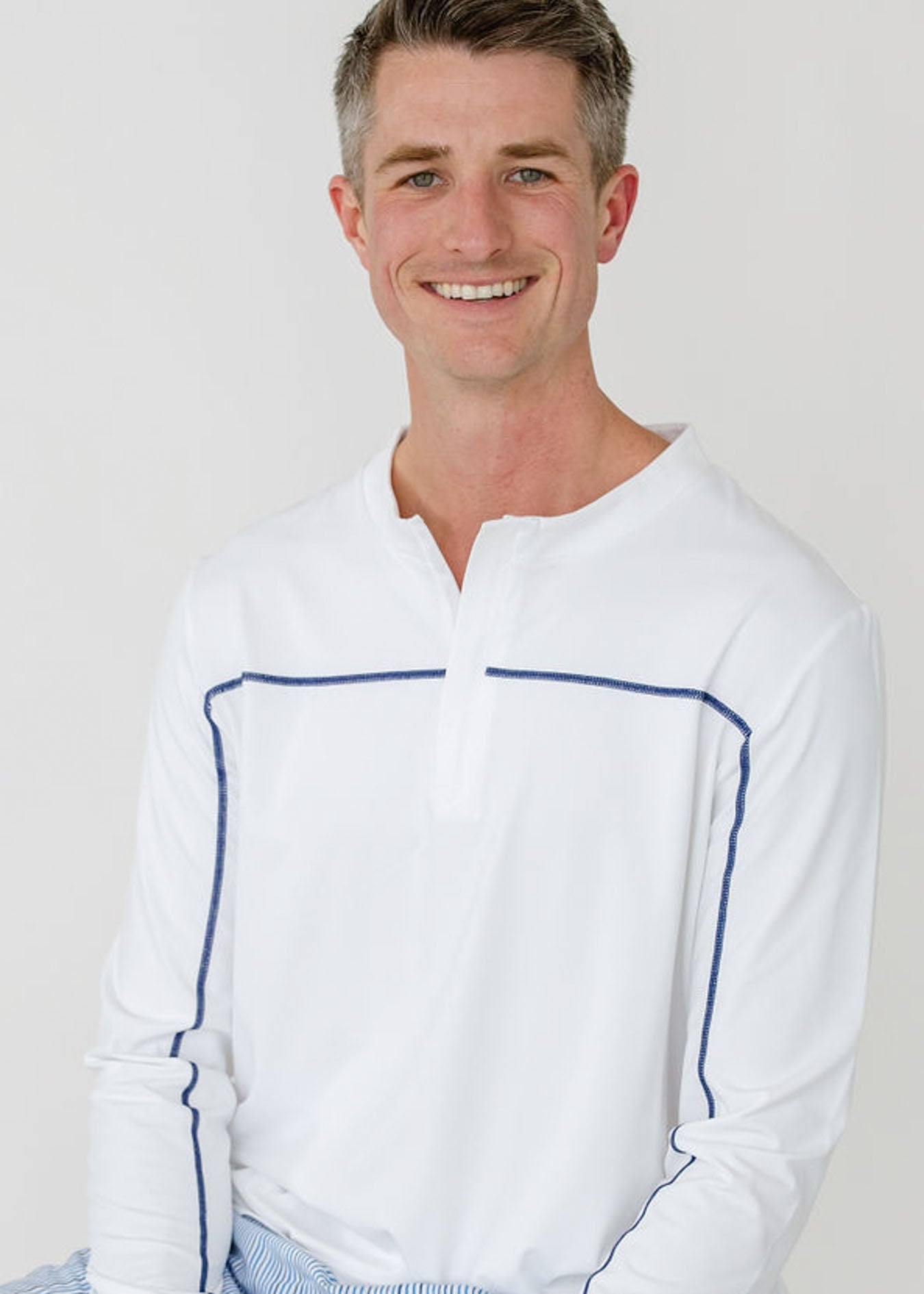 Man wearing a white long-sleeve shirt with blue accents against a plain background
