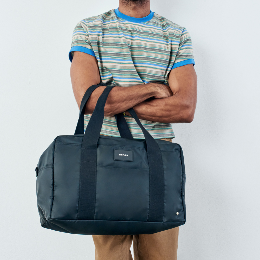 Person holding a navy blue duffel bag with a plain background